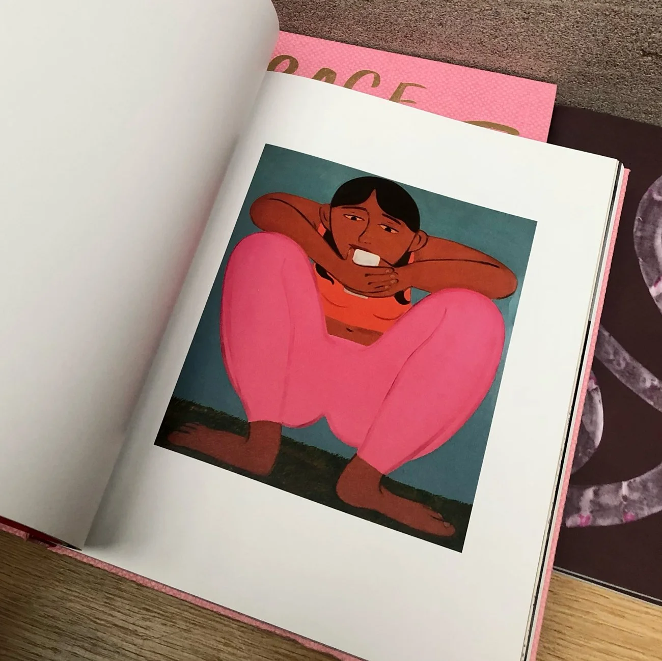 Illustration of a girl sitting with knees drawn up and arms resting on her knees, smiling, wearing pink pants and an orange shirt, with a blue background.