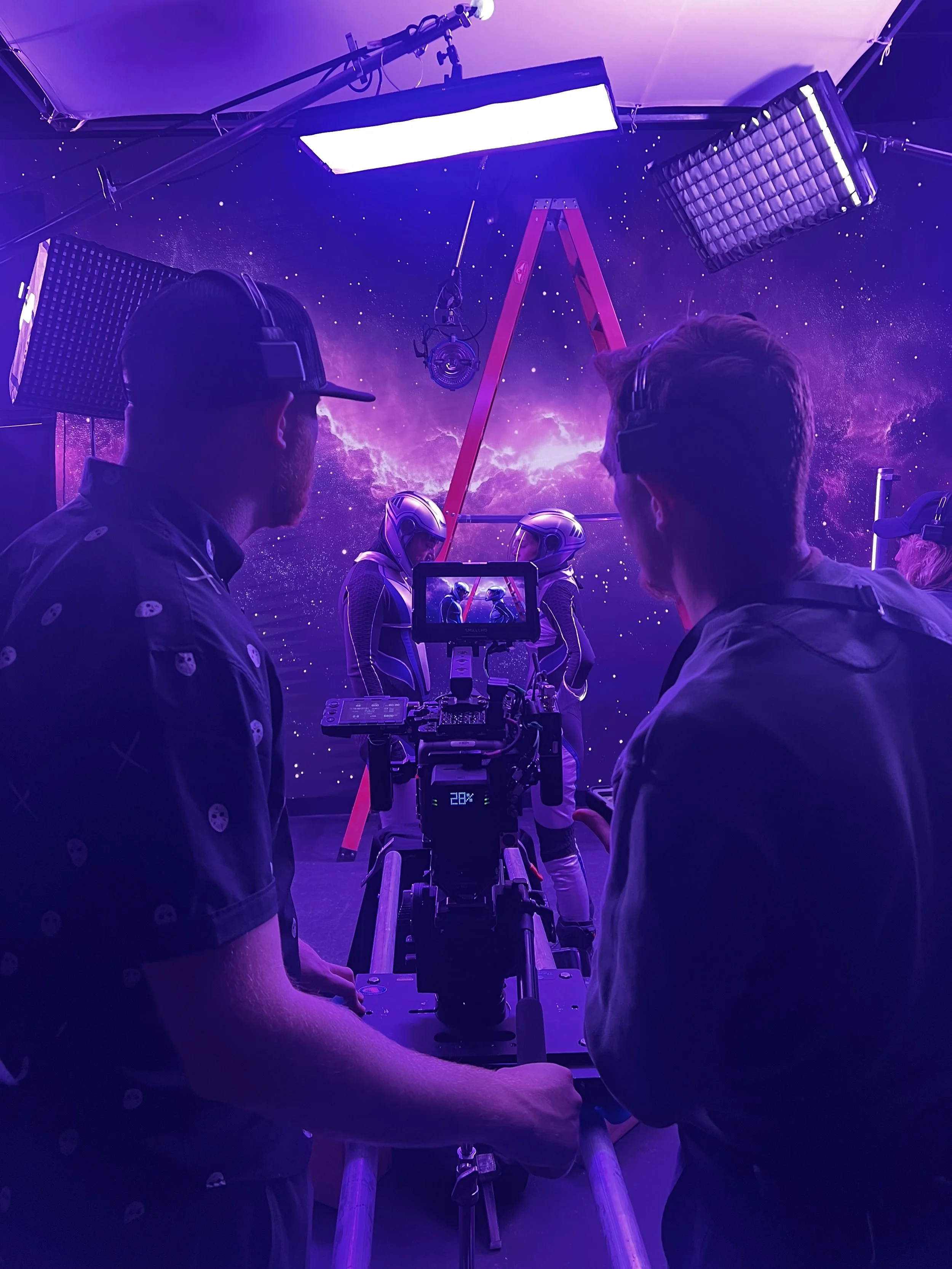 Crew members working with camera equipment in a space-themed studio with a starry galaxy background and purple lighting.