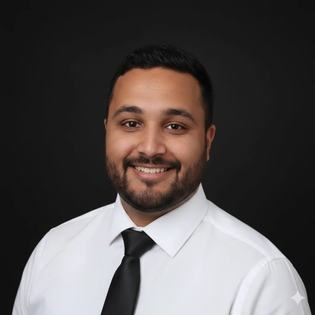 Headshot of a smiling man with dark hair and beard, wearing a white shirt and black tie, against a black background.