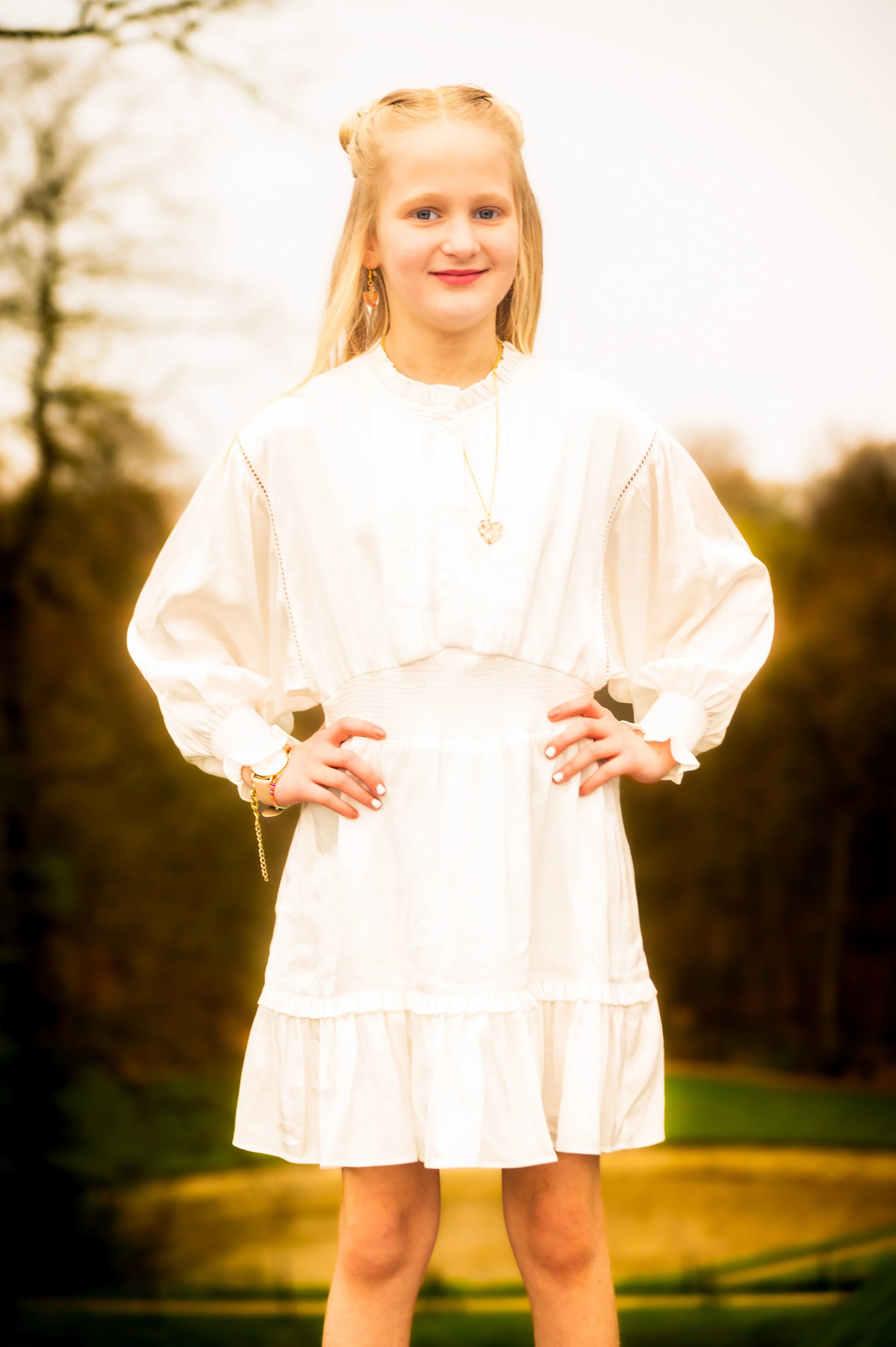 Een jonge vrouw met blond haar die een witte jurk draagt en buiten staat.
