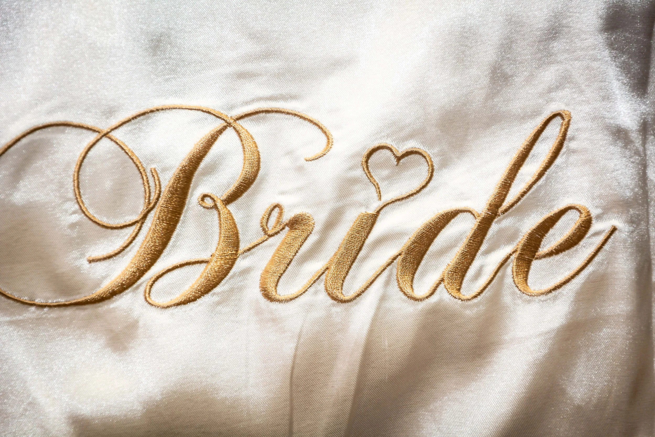 Gouden sierlijke tekst 'Bride' op zijden wittafel