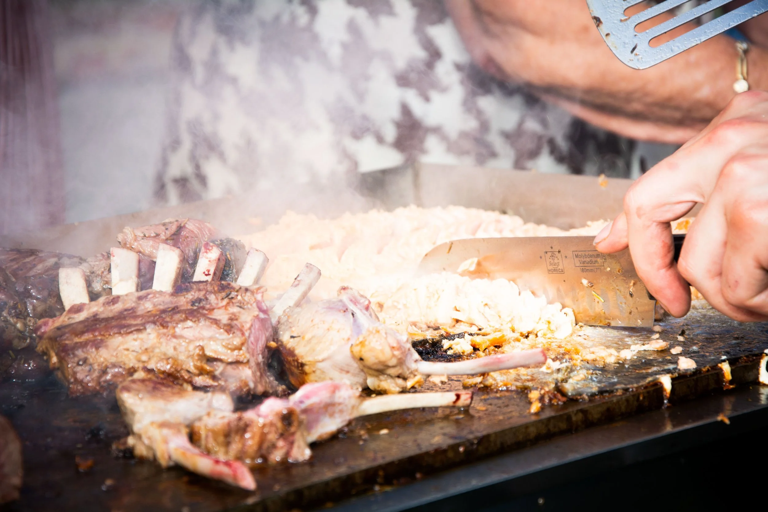 Chef bereidt lamskoteletjes en aardappelpuree op een grill met rook.