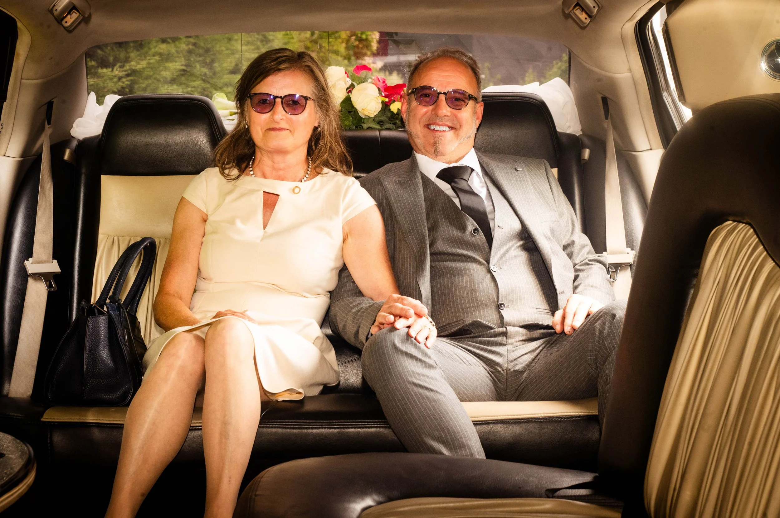 Een man en een vrouw zitten samen in de achterbank van een limousine, ze dragen formele kleding en glimlachen.