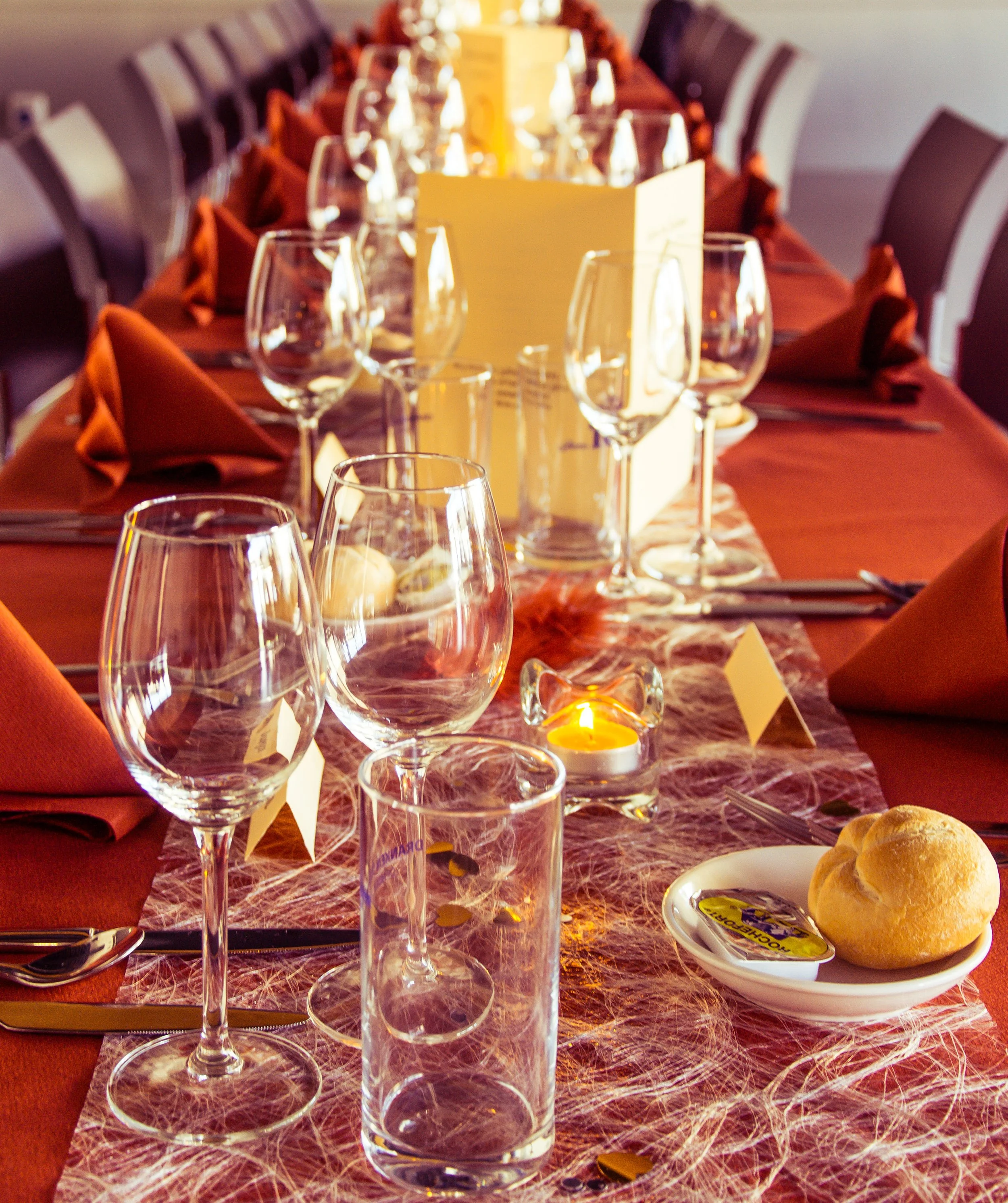 Een feestelijke gedekte tafel met glaswerk, borden, bestek, een broodje, een kaars en een tafelmenu, klaar voor een etentje.
