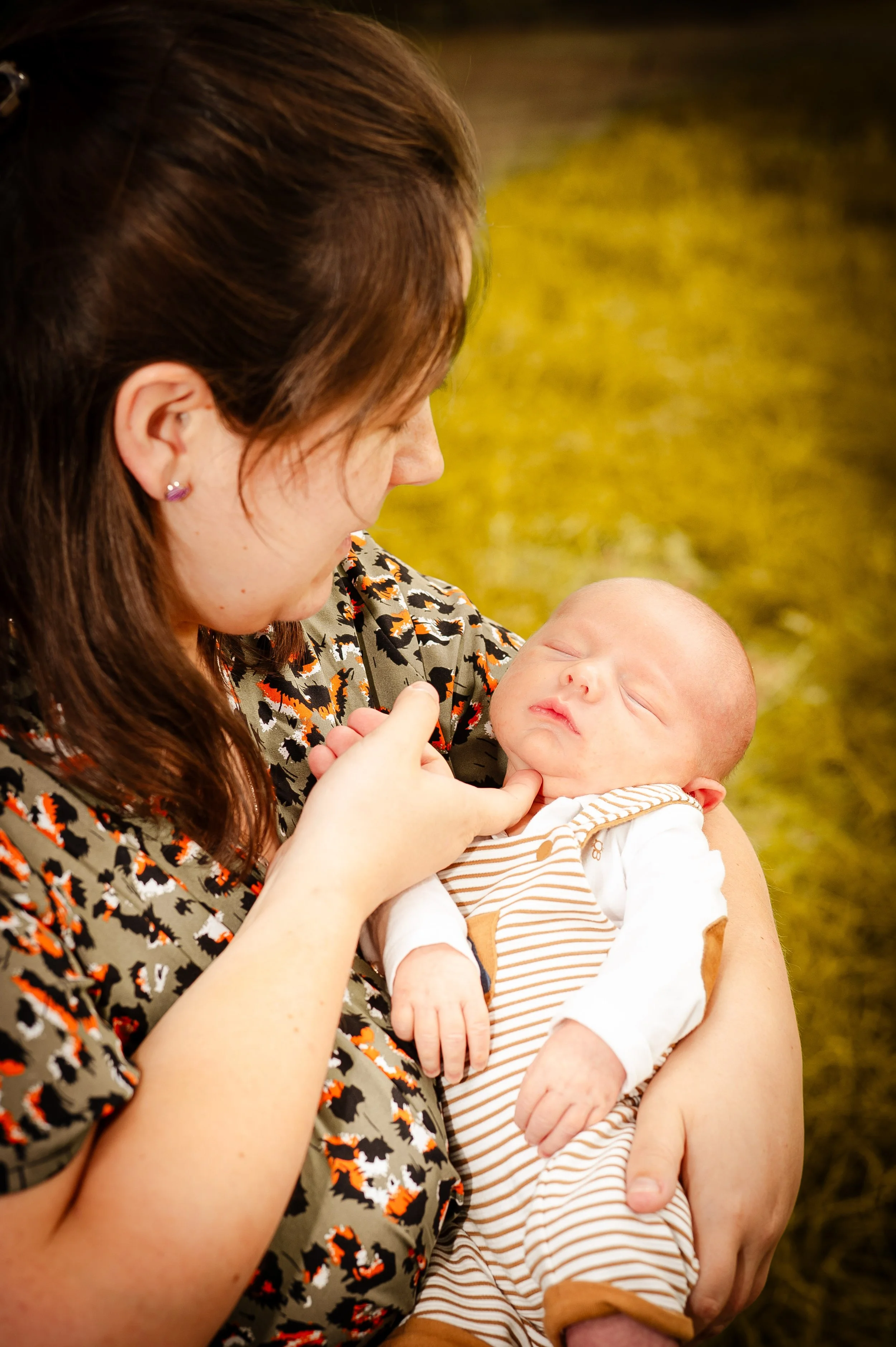 Vrouw houdt slapende baby in haar armen buiten, groene achtergrond.