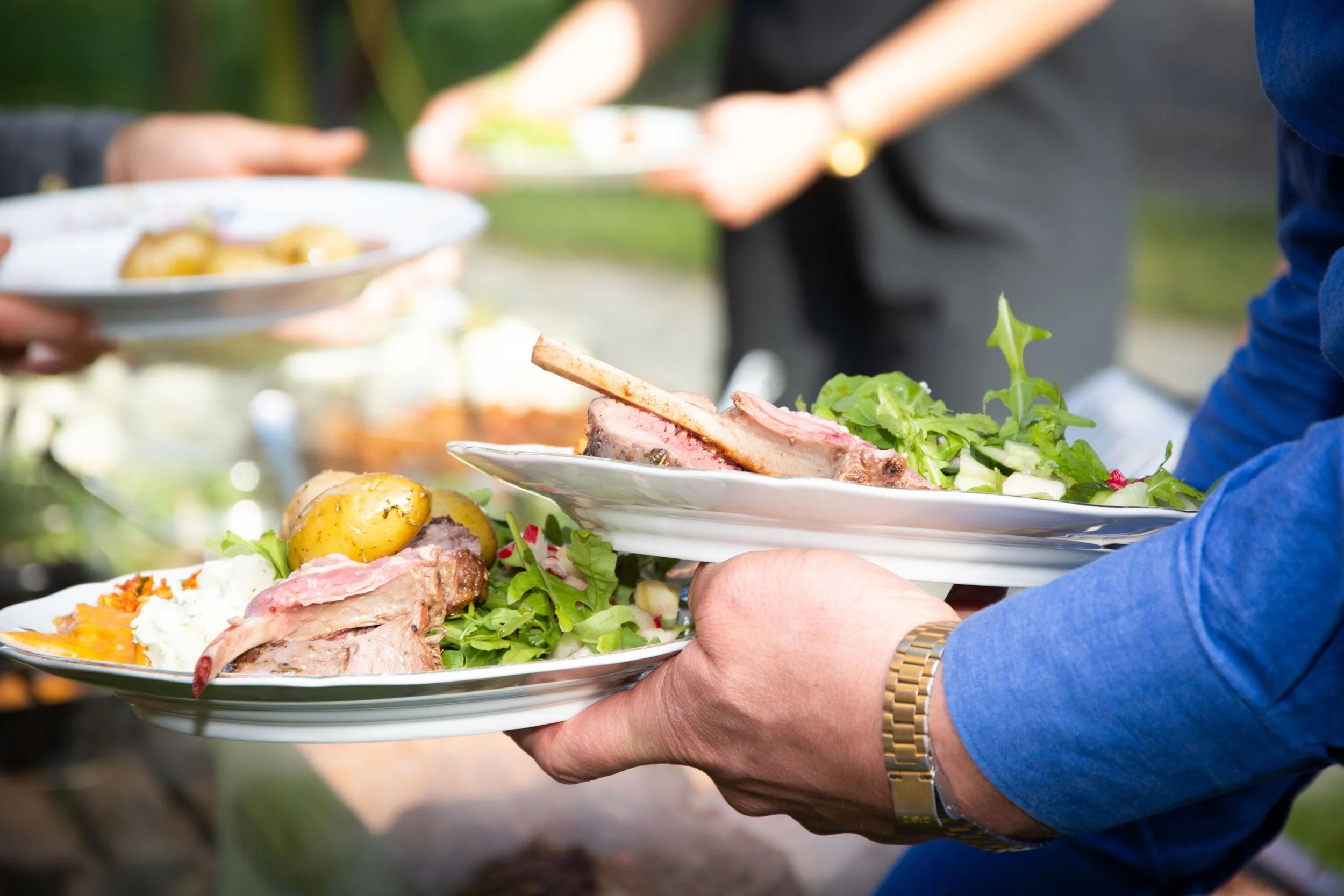 Mensen serveren vlees, aardappels en salade op een witte schaal tijdens een barbecue.