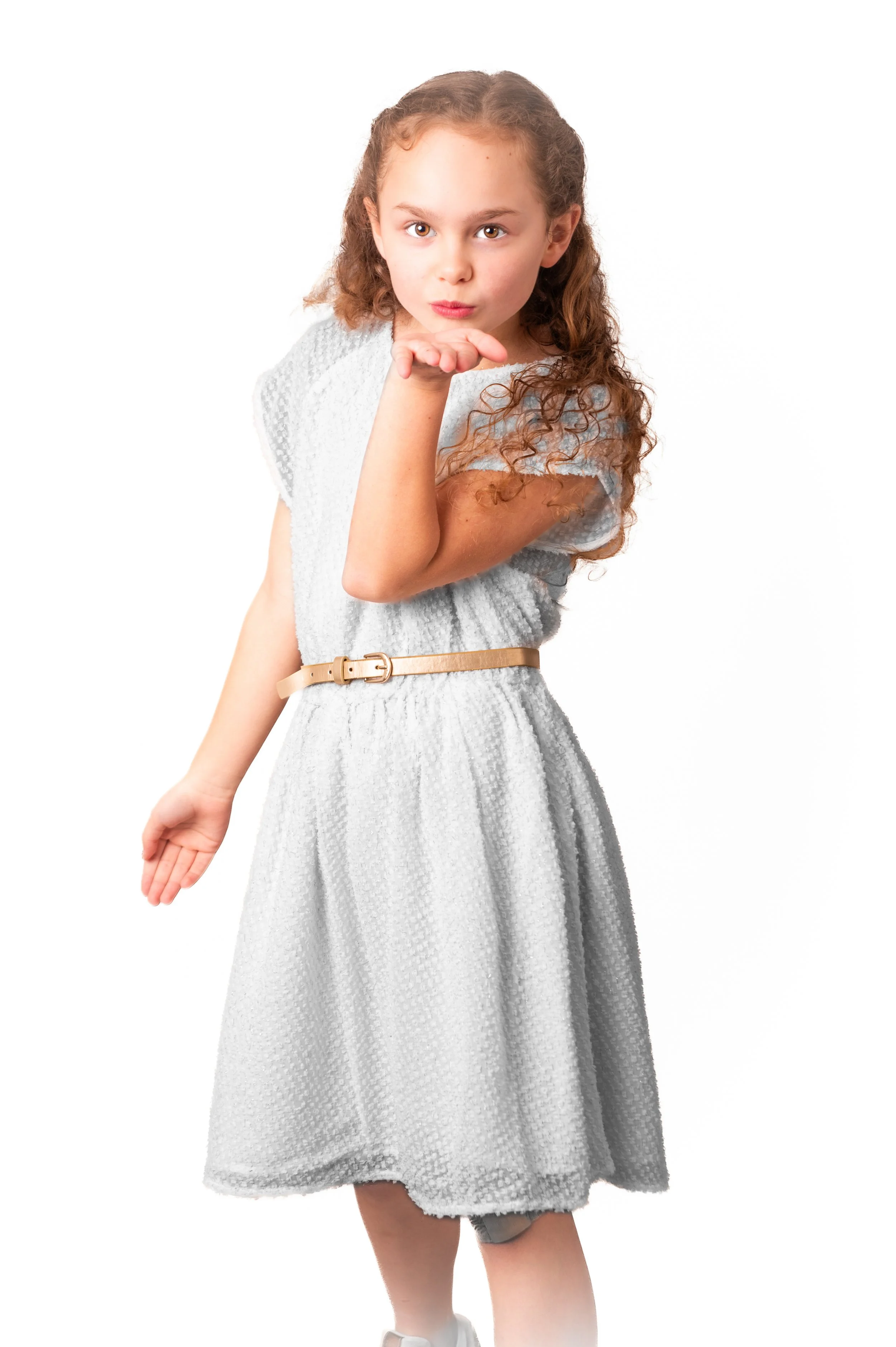 een jonge vrouw met lang, krullend, bruin haar die een knipoog geeft en een lippenkus stuurt terwijl ze haar hand naar haar lippen brengt, gekleed in een witte jurk met een beige riem