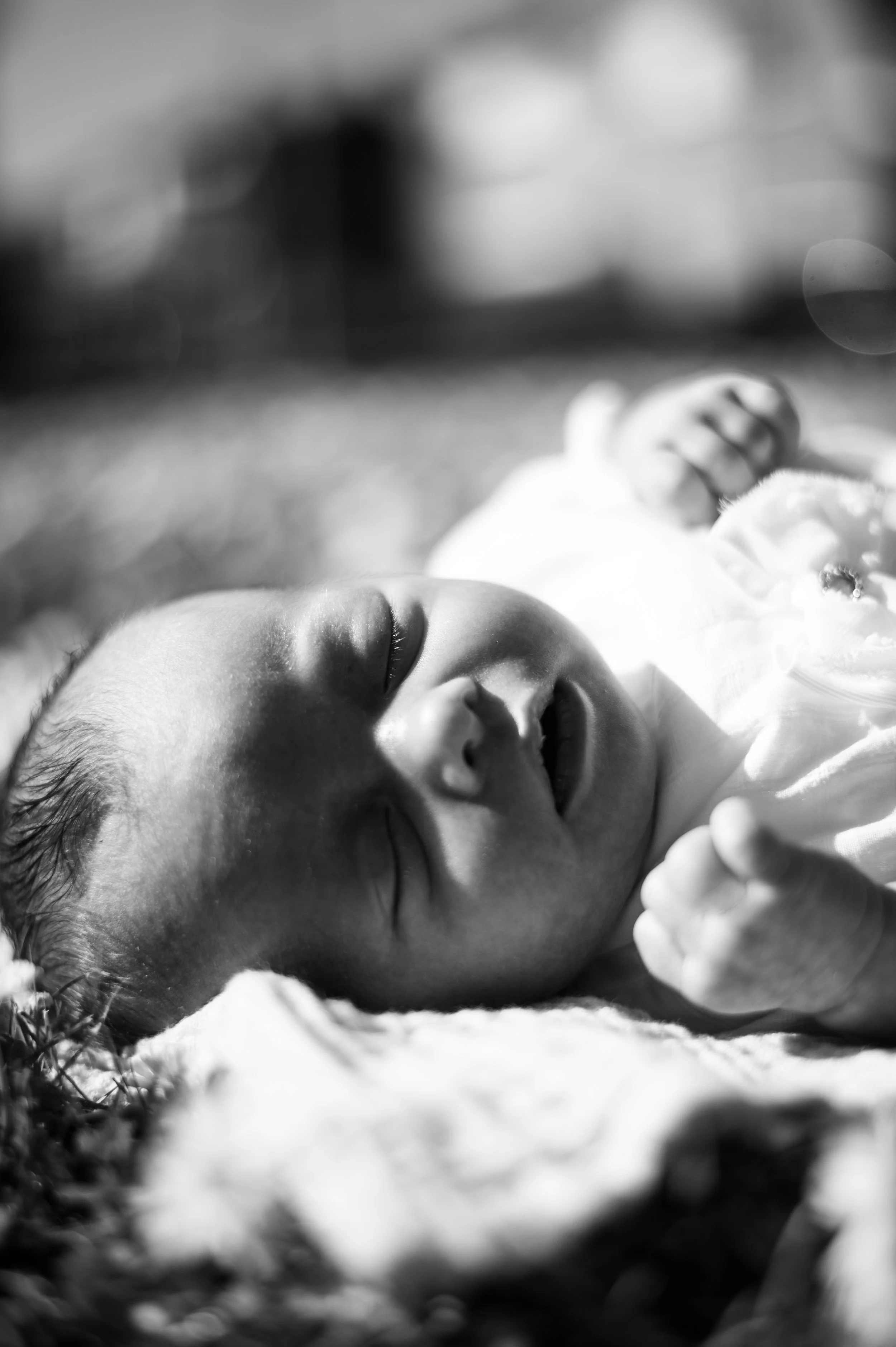 Zwarte en witte foto van slapende baby met gesloten ogen op een draagbare ondergrond, buiten met natuurlijke lichtinval.