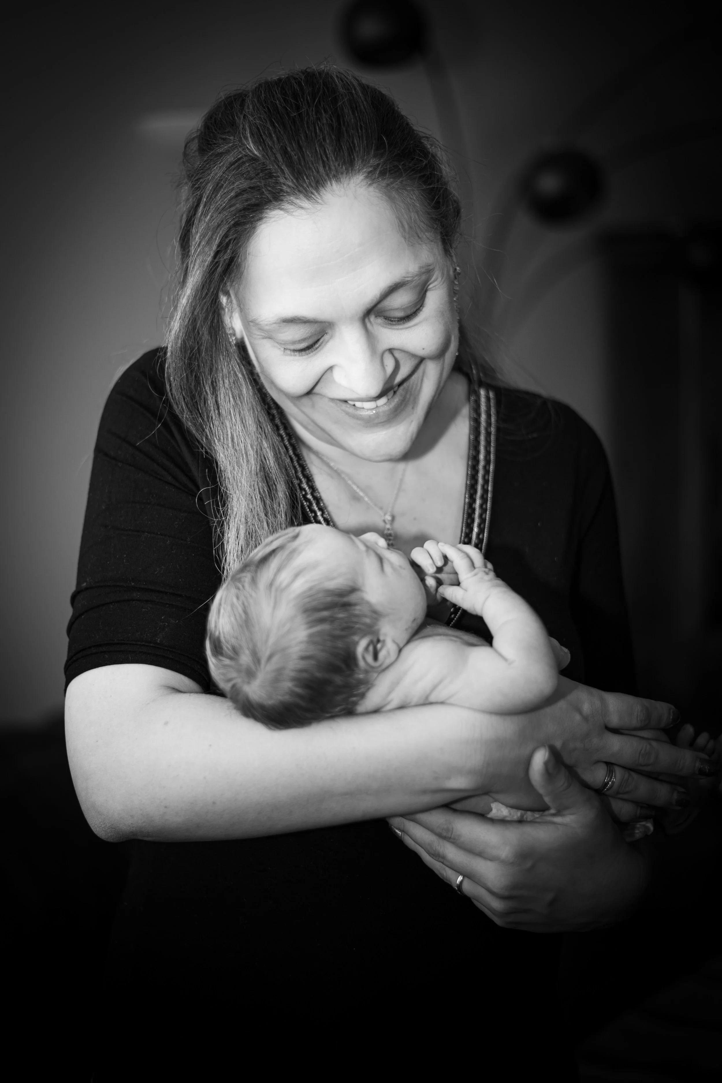 Zwarte en witte foto van een vrouw die een slapende baby vasthoudt, glimlachend naar de baby.