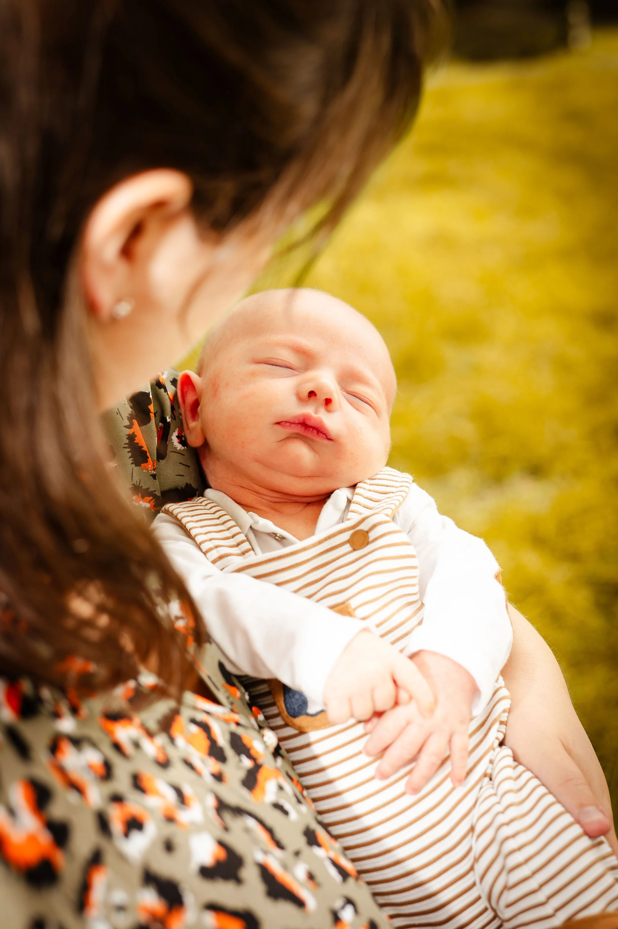 Close-up van een slapende baby die door een vrouw wordt vastgehouden, met een groene achtergrond.