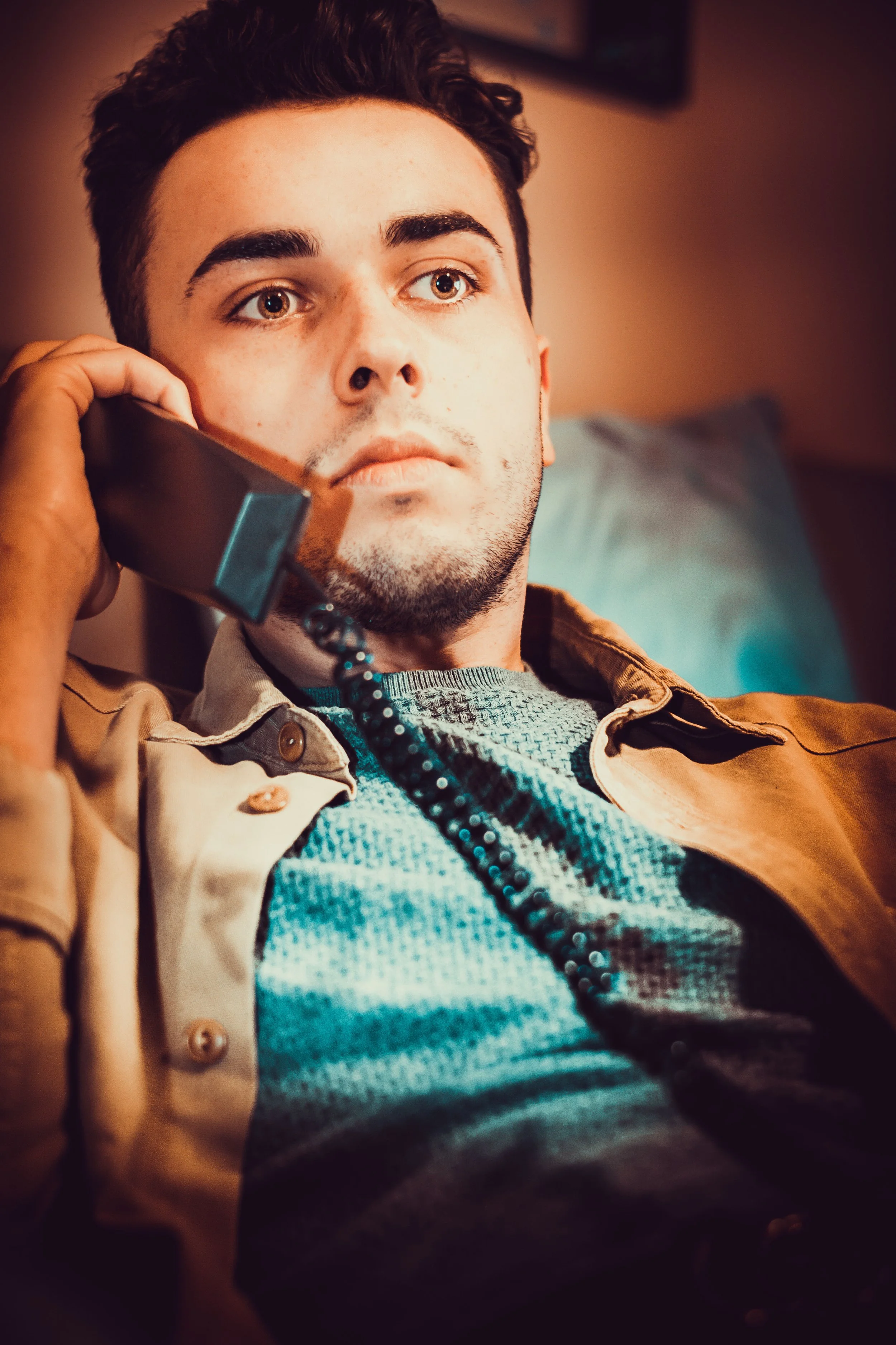 Man ligt op bed en spreekt op de telefoon met een serieuze uitdrukking.