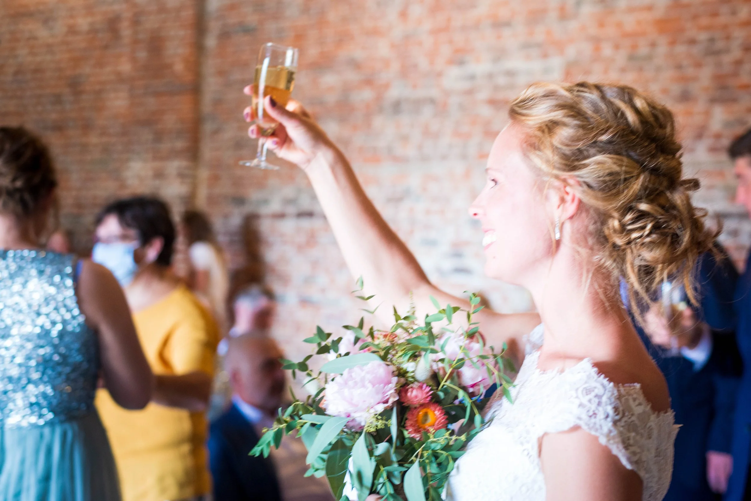Vrouw die een glas champagne heft op een feest met andere mensen, een vrouw met een gele jurk en een vrouw met een sprankeljurk.