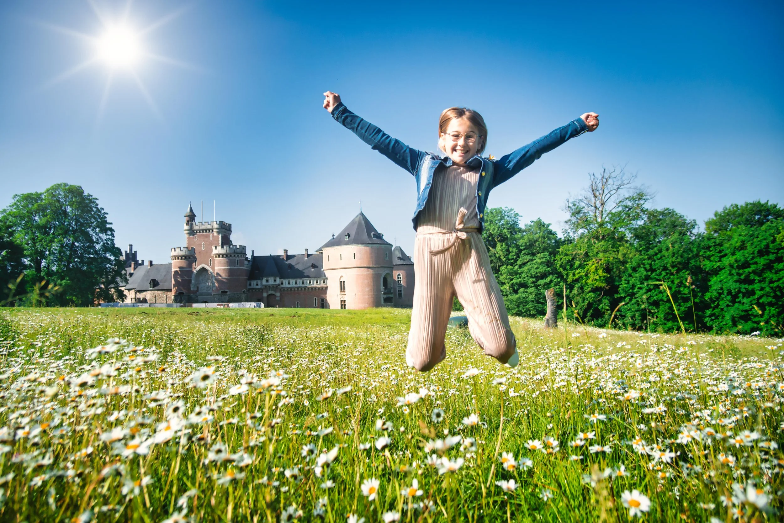 Vrolijke vrouw springt in een veld met bloemen voor een kasteel onder een blauwe lucht