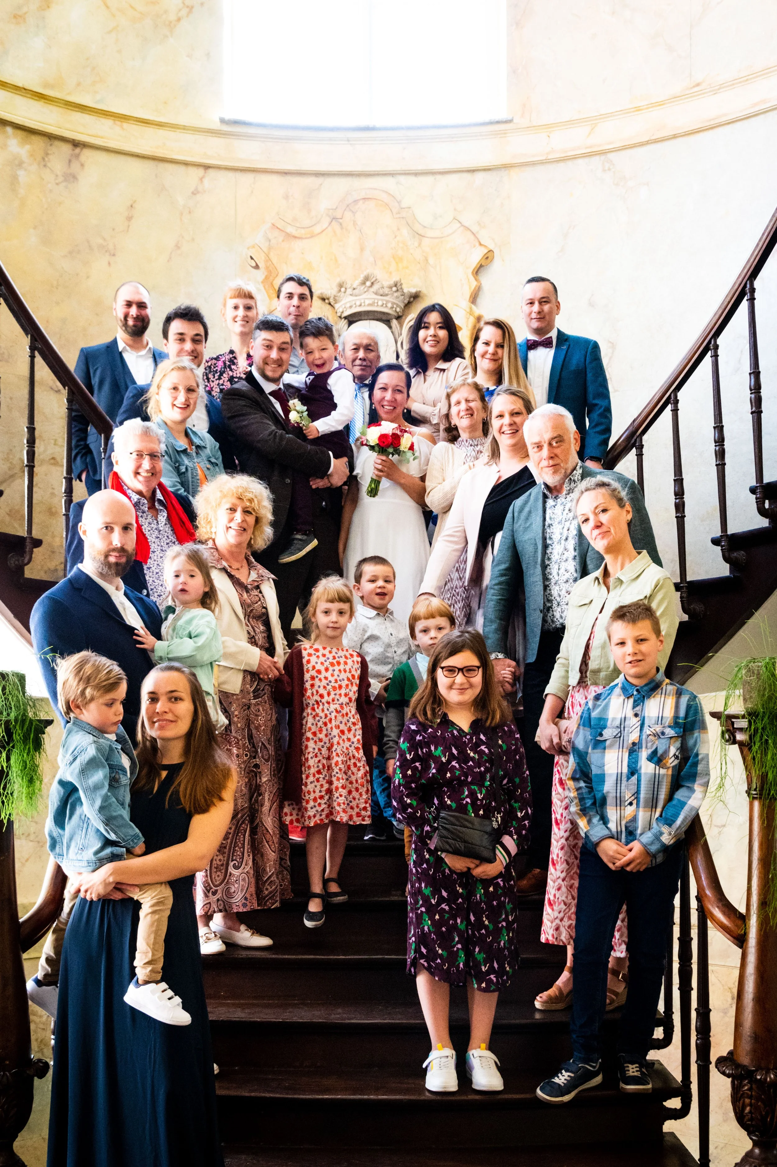 Een grote groep mensen posing op een houten trap tijdens een feest, met een bruid en bruidegom in het midden.