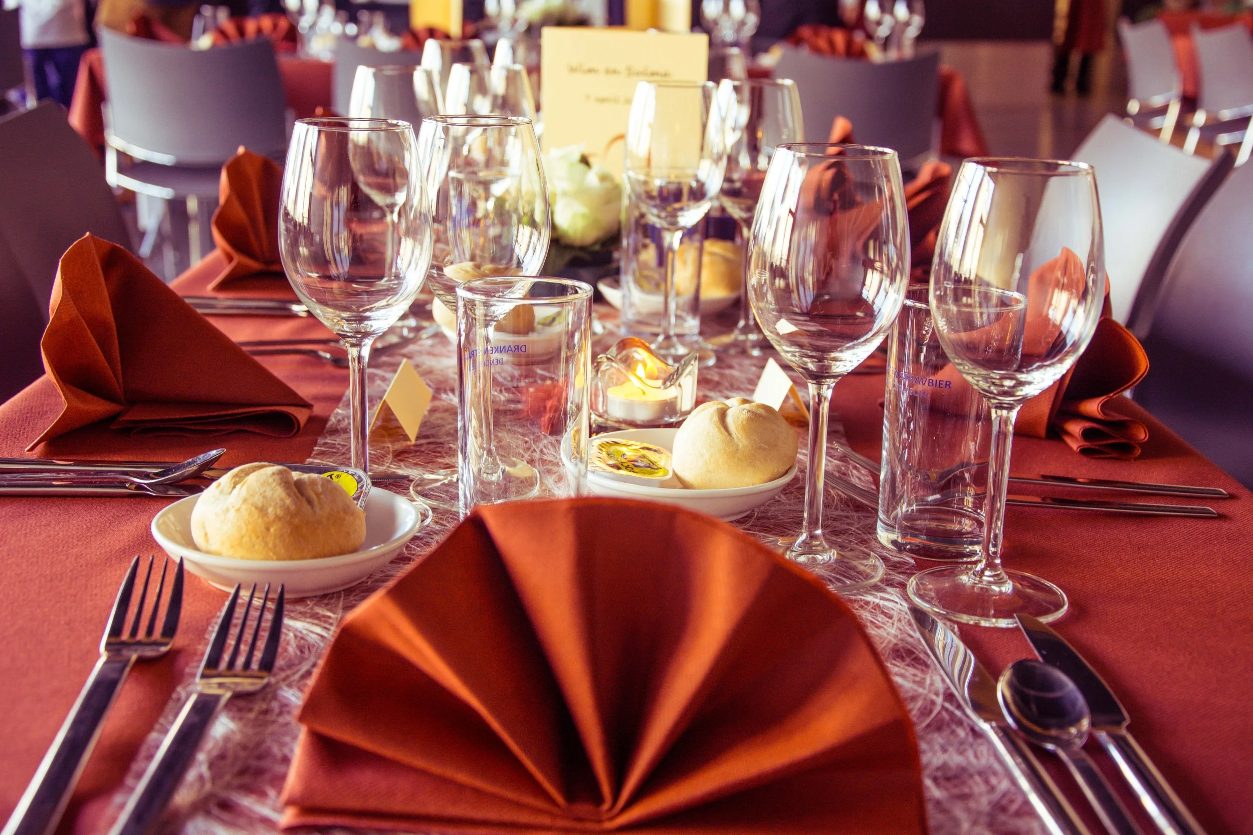 Een feestelijk gedekte tafel met glazen, borden met broodjes, roodgekleurde servetten en bestek, klaar voor een diner.