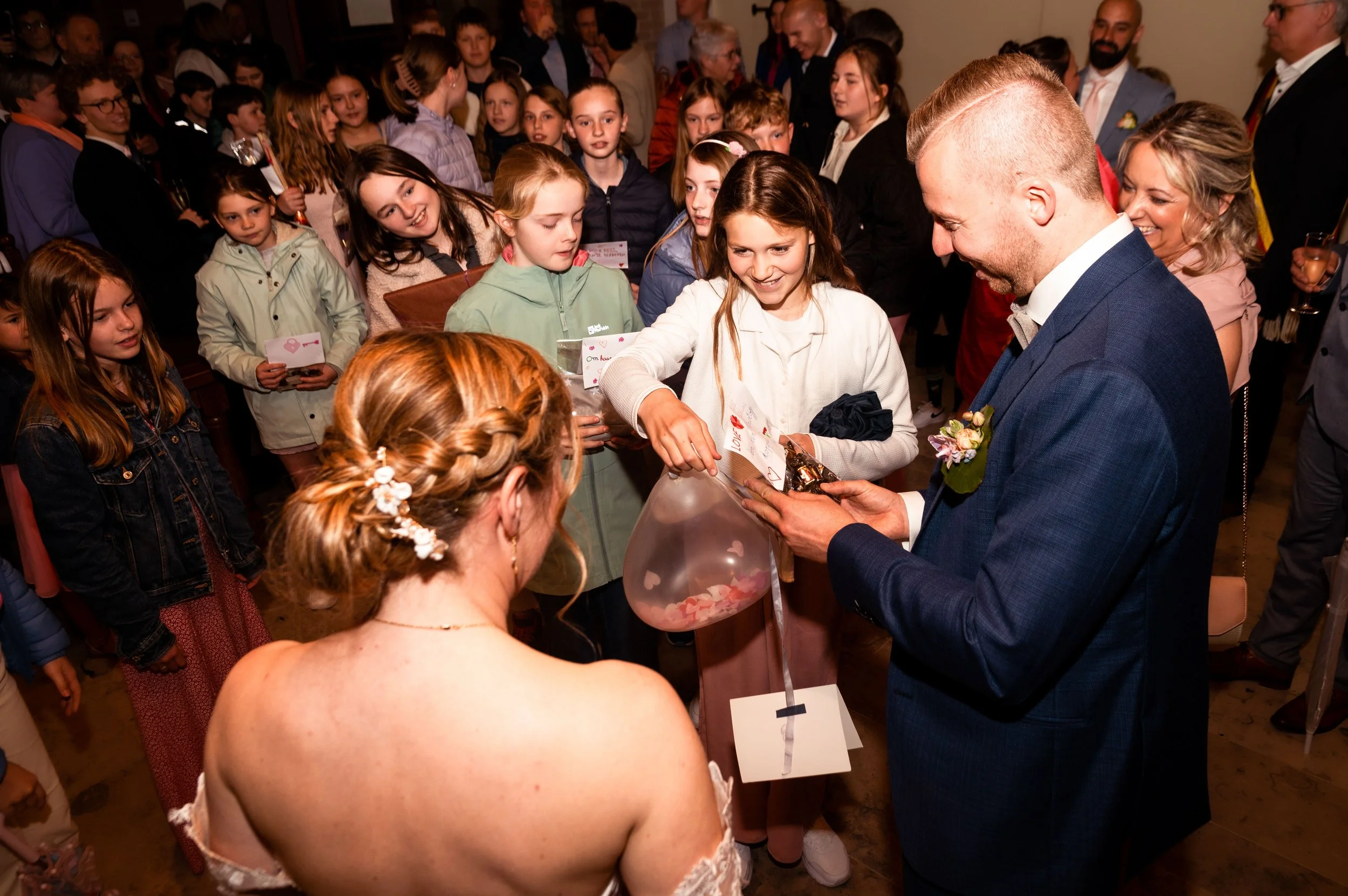 Kinderen en volwassenen verzamelen zich rondom een man die cadeautjes uitdeelt, er is feeststemming.