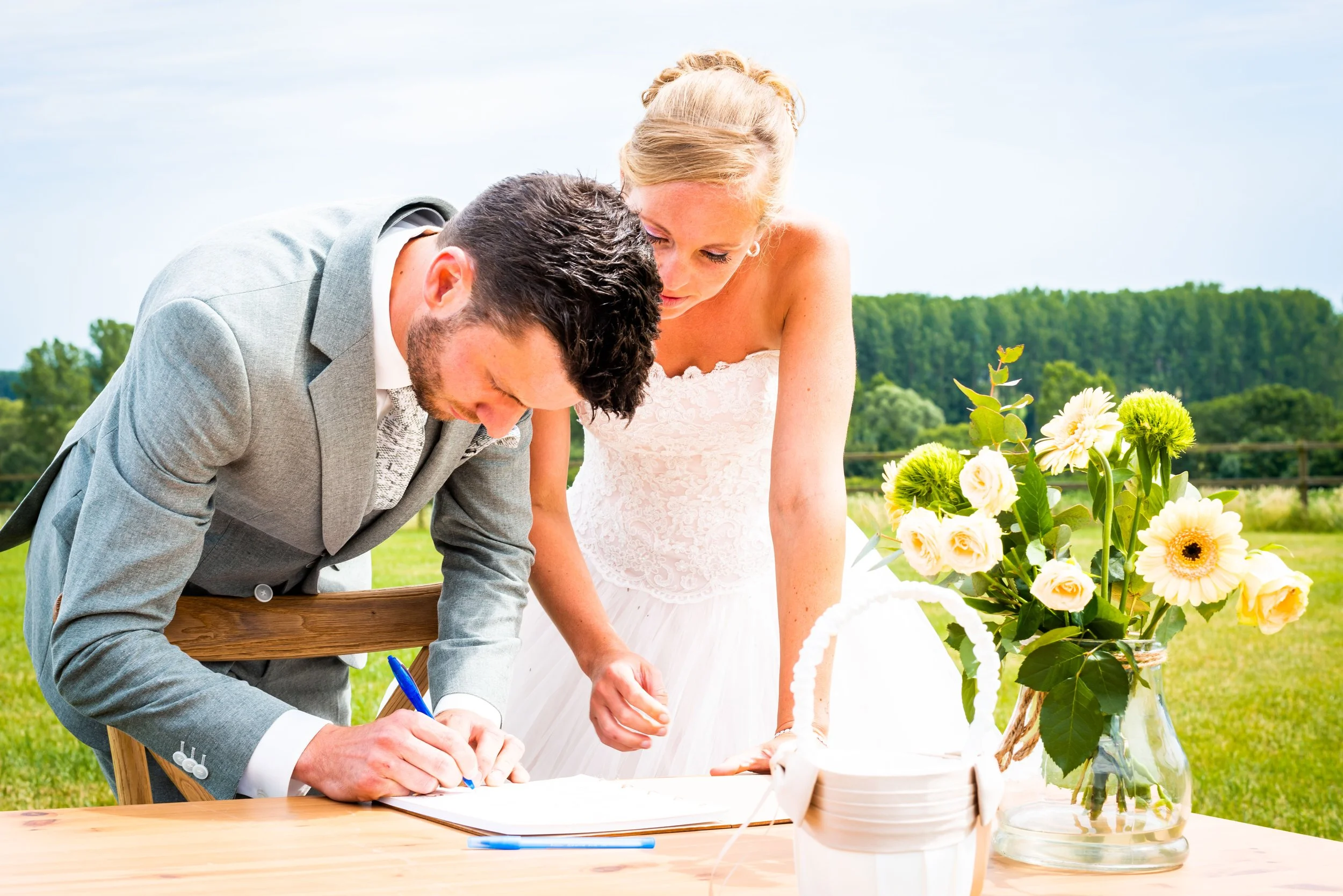 Een man en vrouw ondertekenen een document buiten, met een bloemstuk op tafel.