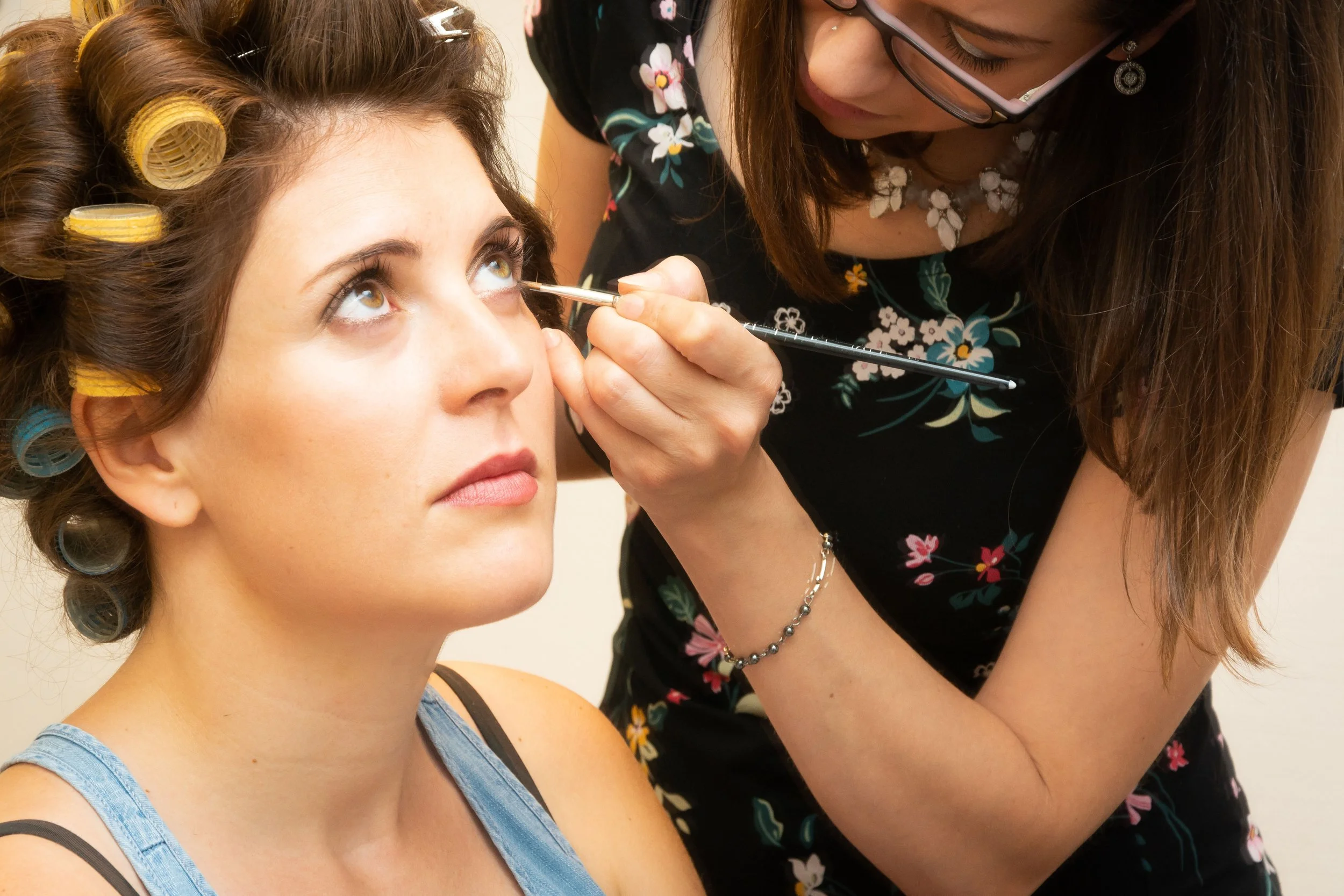 Een vrouw die make-up aan het aanbrengen is op een andere vrouw die haar hoofd naar achteren kantelt.