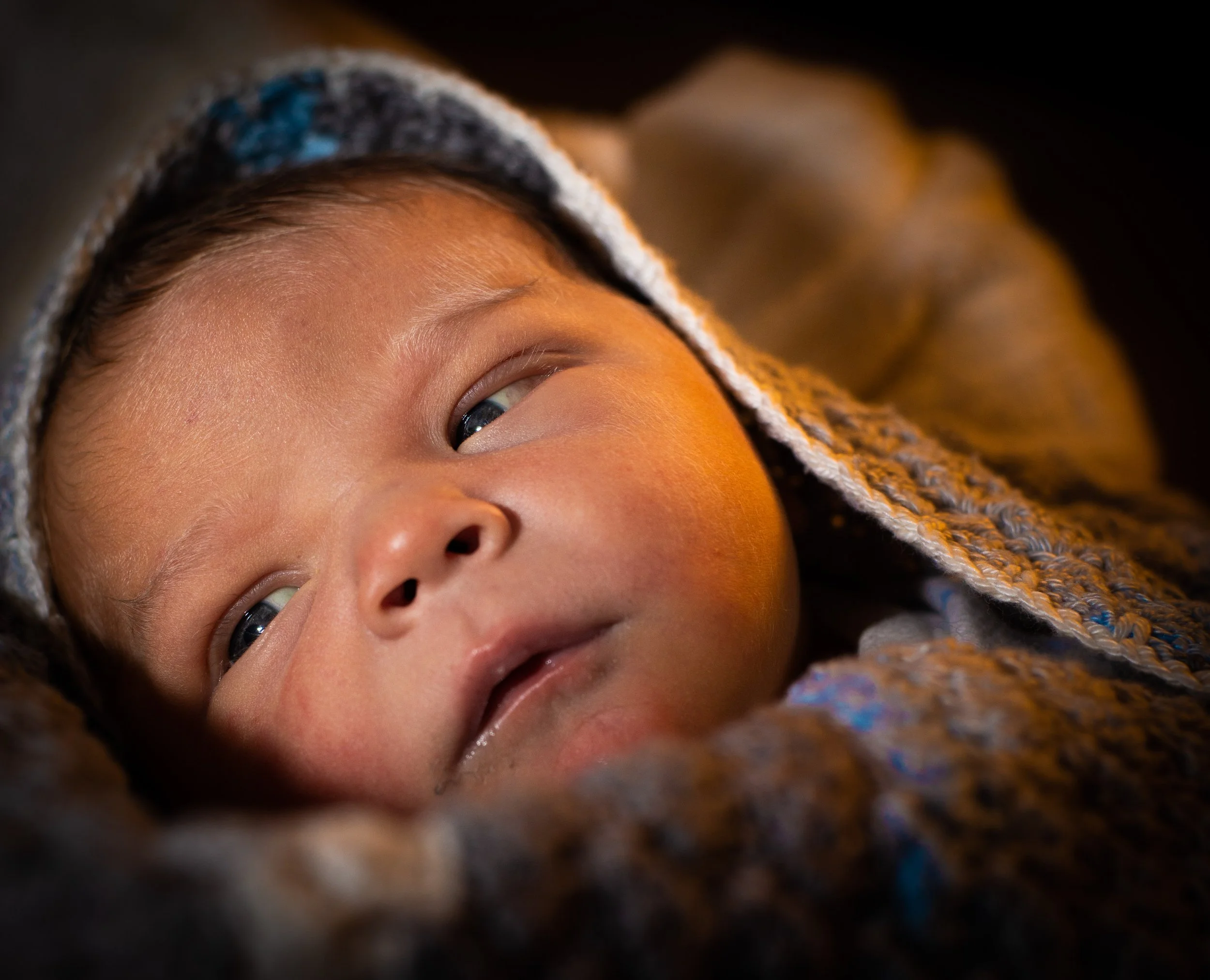 Close-up van een baby met blauwe ogen, ingedekt met een gebreide doek.