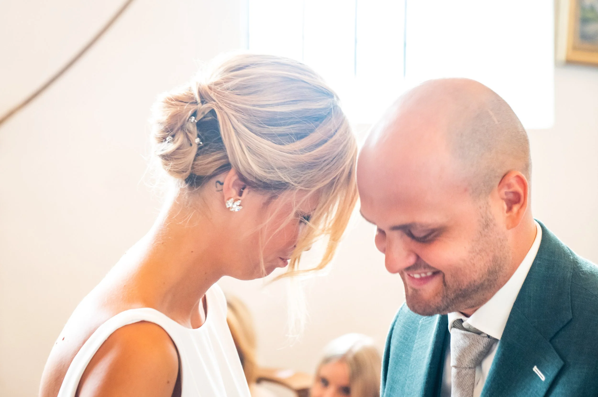 Een bruid en bruidegom staan met hun voorhoofden tegen elkaar, een intiem moment van emotie en liefde tijdens een huwelijk, binnen.