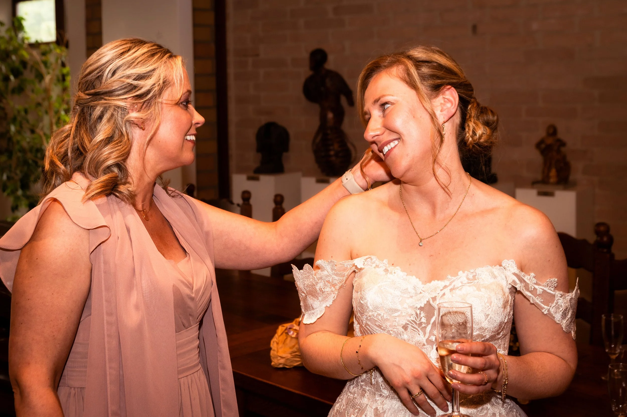 Twee vrouwen op een feest, de ene vrouw raakt de andere aan haar gezicht terwijl ze lachen.