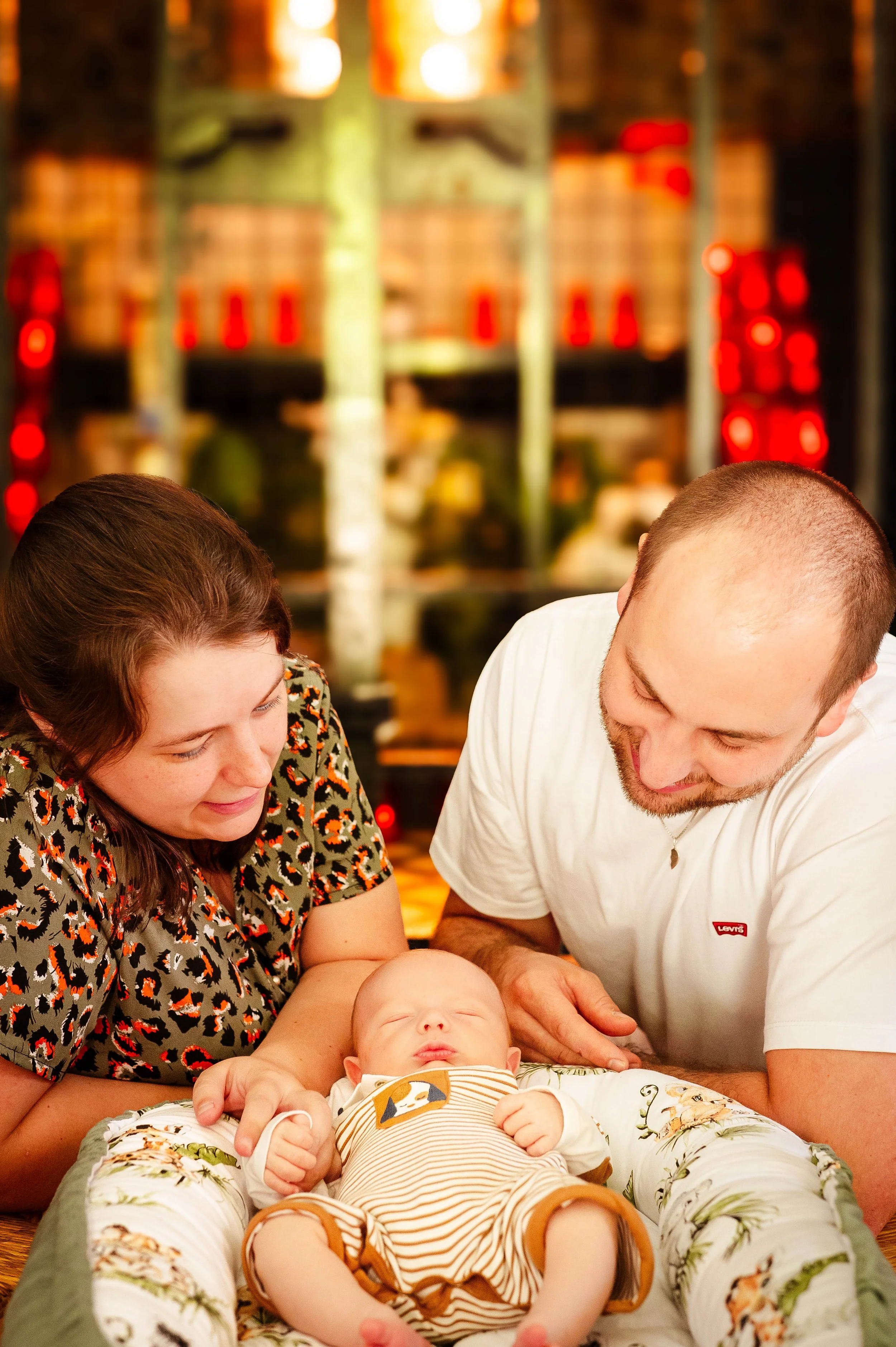 Een jonge familie, bestaande uit een man, een vrouw en een baby, die samen naar de baby kijken in een gezellige binnenlocatie
