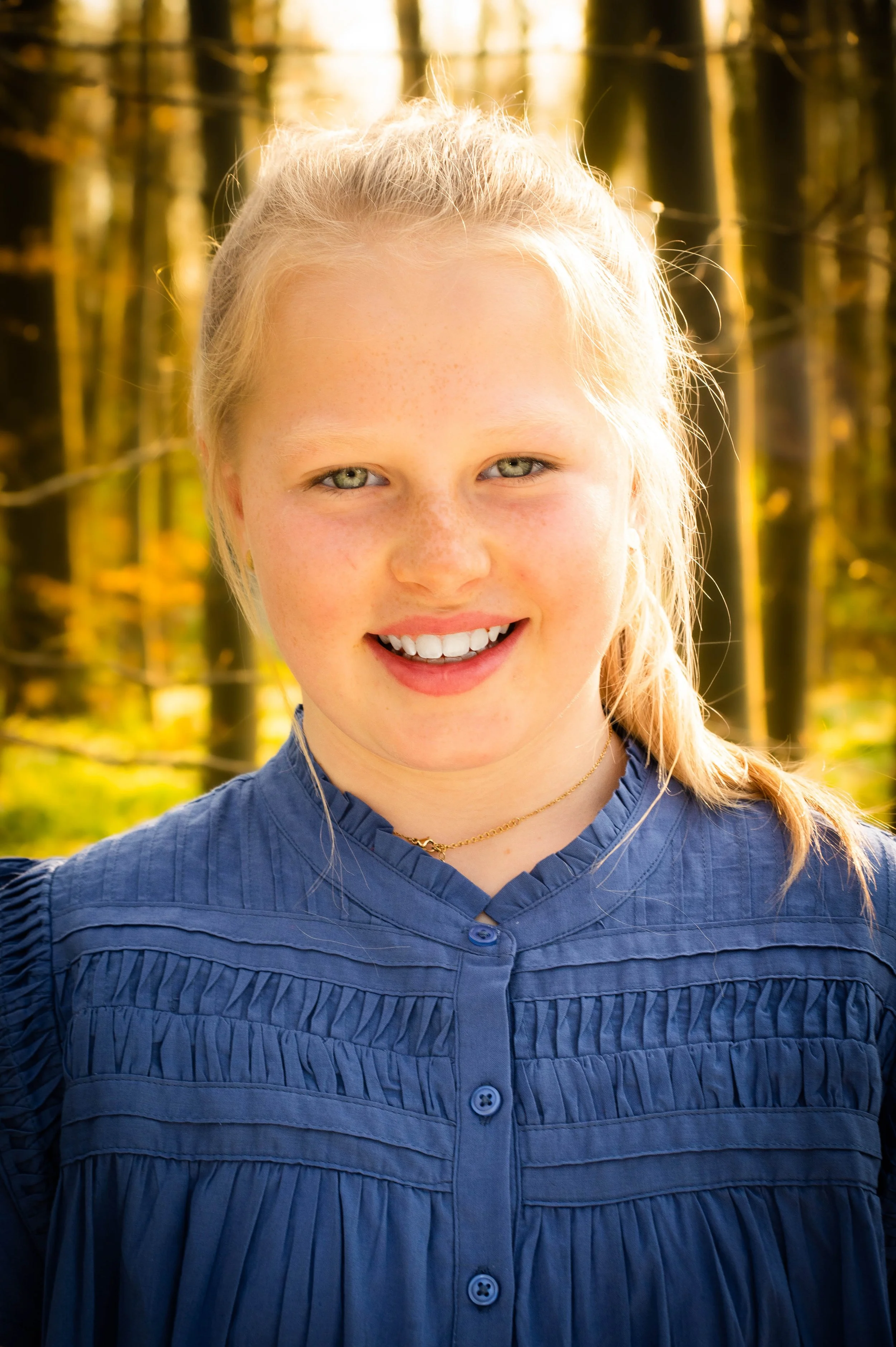 Close-up van een lachende jonge vrouw met blonde haar in een bos bij zonsondergang.
