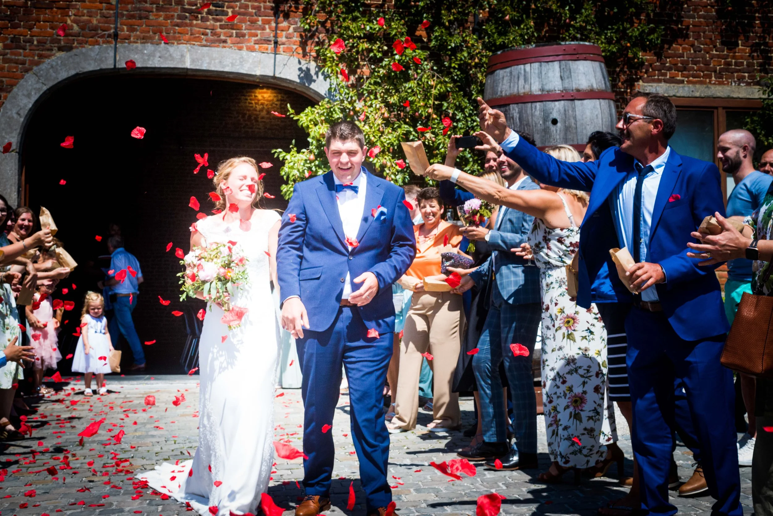 Bruid en bruidegom lopen door een route van gasten die rozenblaadjes over hen strooien tijdens een huwelijksfeest buiten.