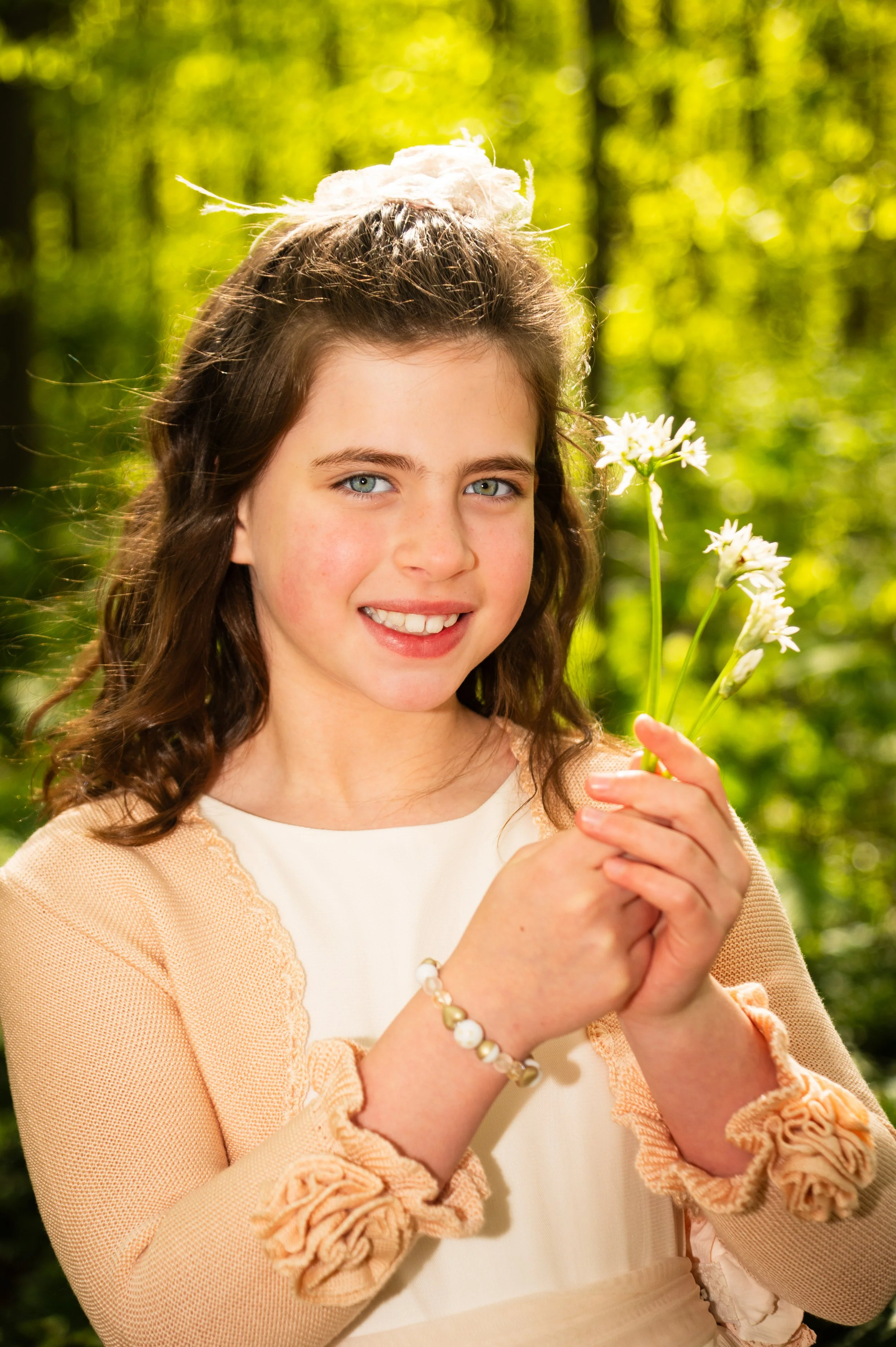 Lachend meisje met blauwe ogen houdt witte bloemen vast in een bos met groene bladeren.