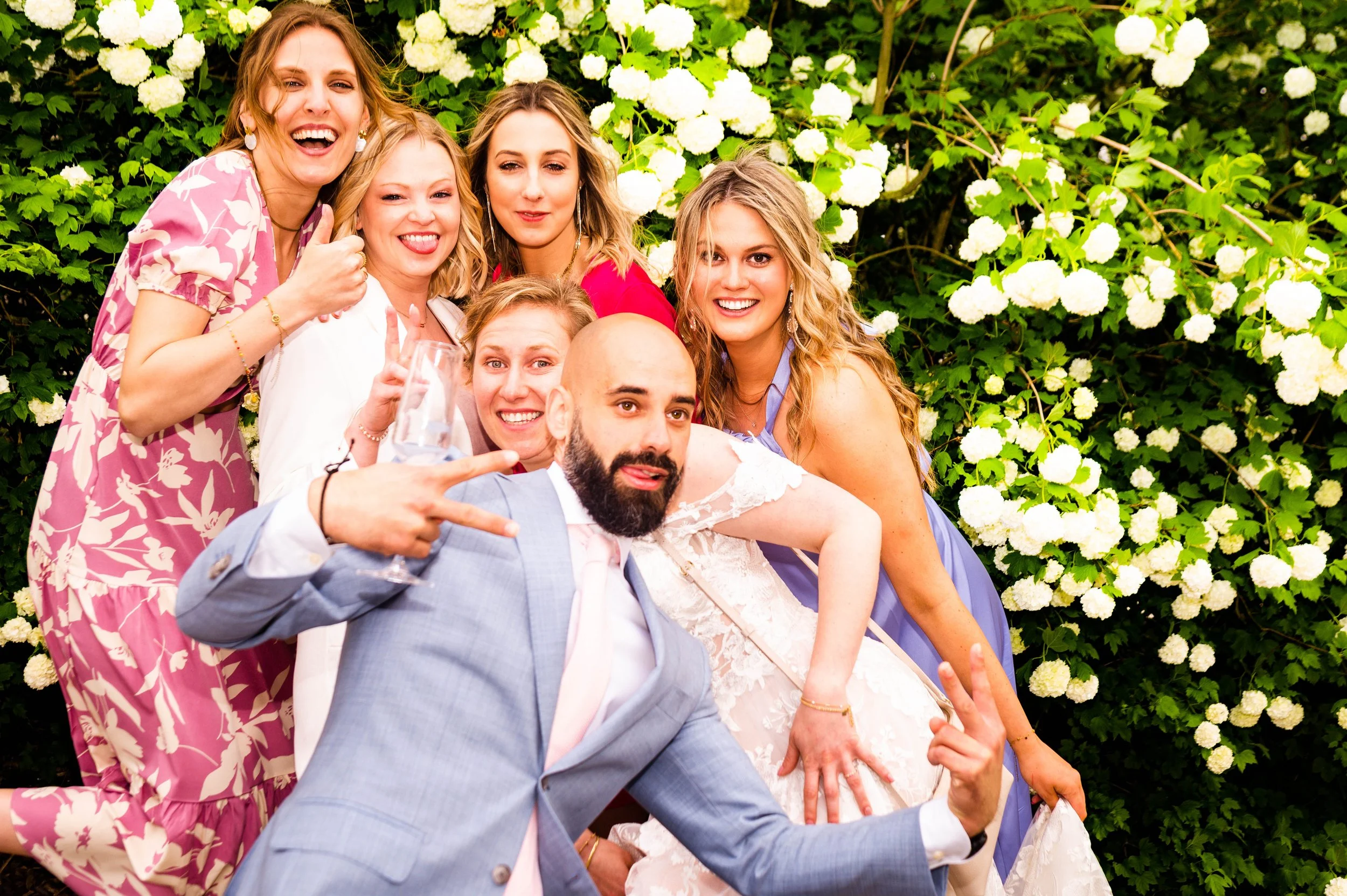Een groep vrienden poseren vrolijk voor een bloeiende witte hortensia struik tijdens een feestelijke gelegenheid.
