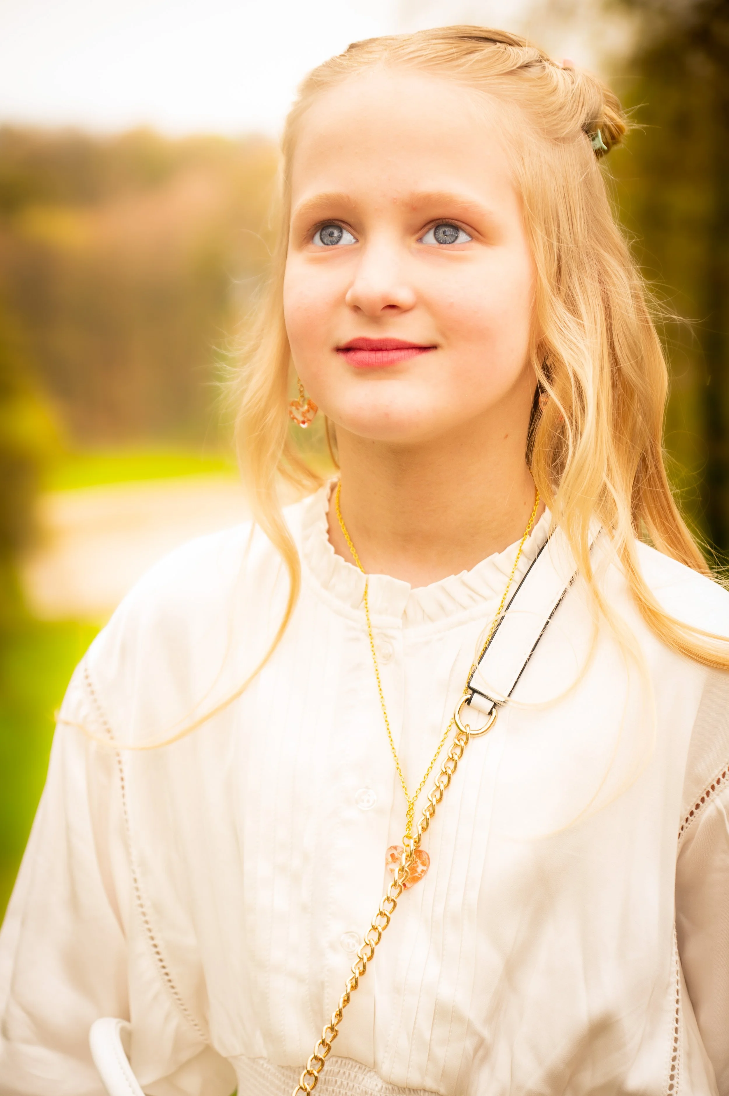Portret van een jonge vrouw met blond haar, blauwe ogen en lichte huid, buiten in een parkachtige omgeving.