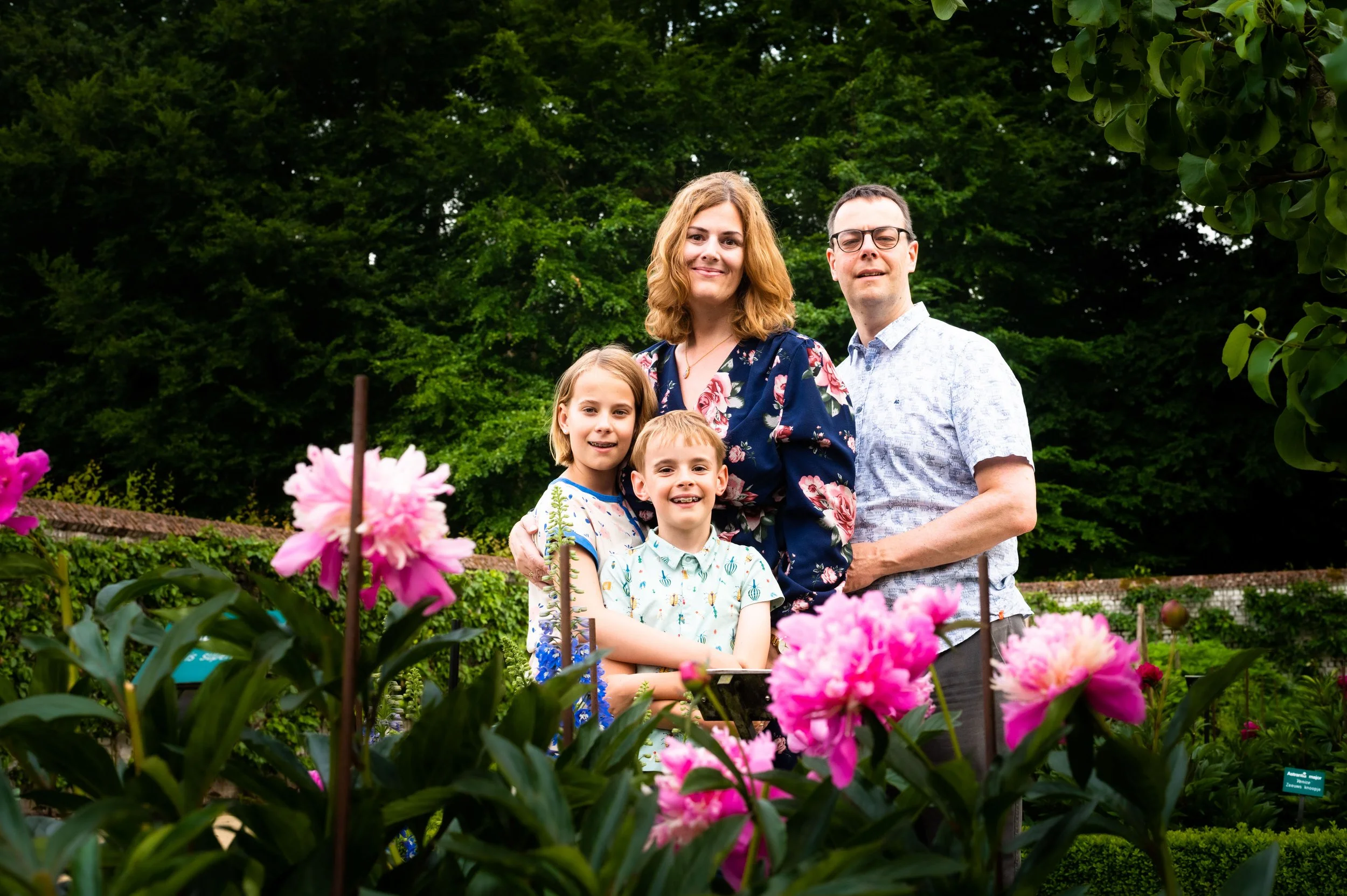 Gezin bestaande uit twee kinderen, een vrouw en een man poseert in een tuin met roze bloemen.