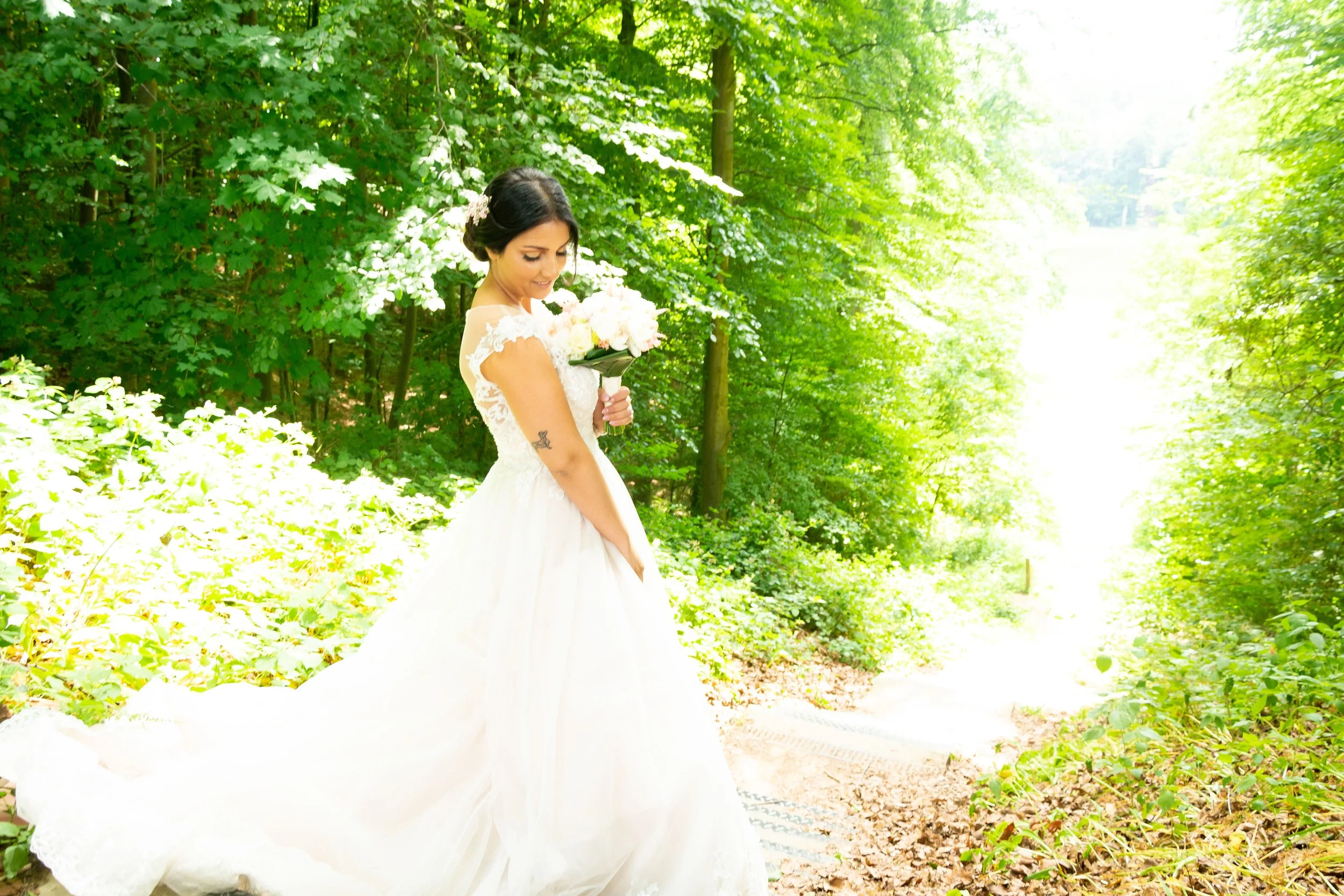 Vrouw in witte trouwjurk met bloem in haar haar, wandelend in een groen bos en de bloemen vasthoudend