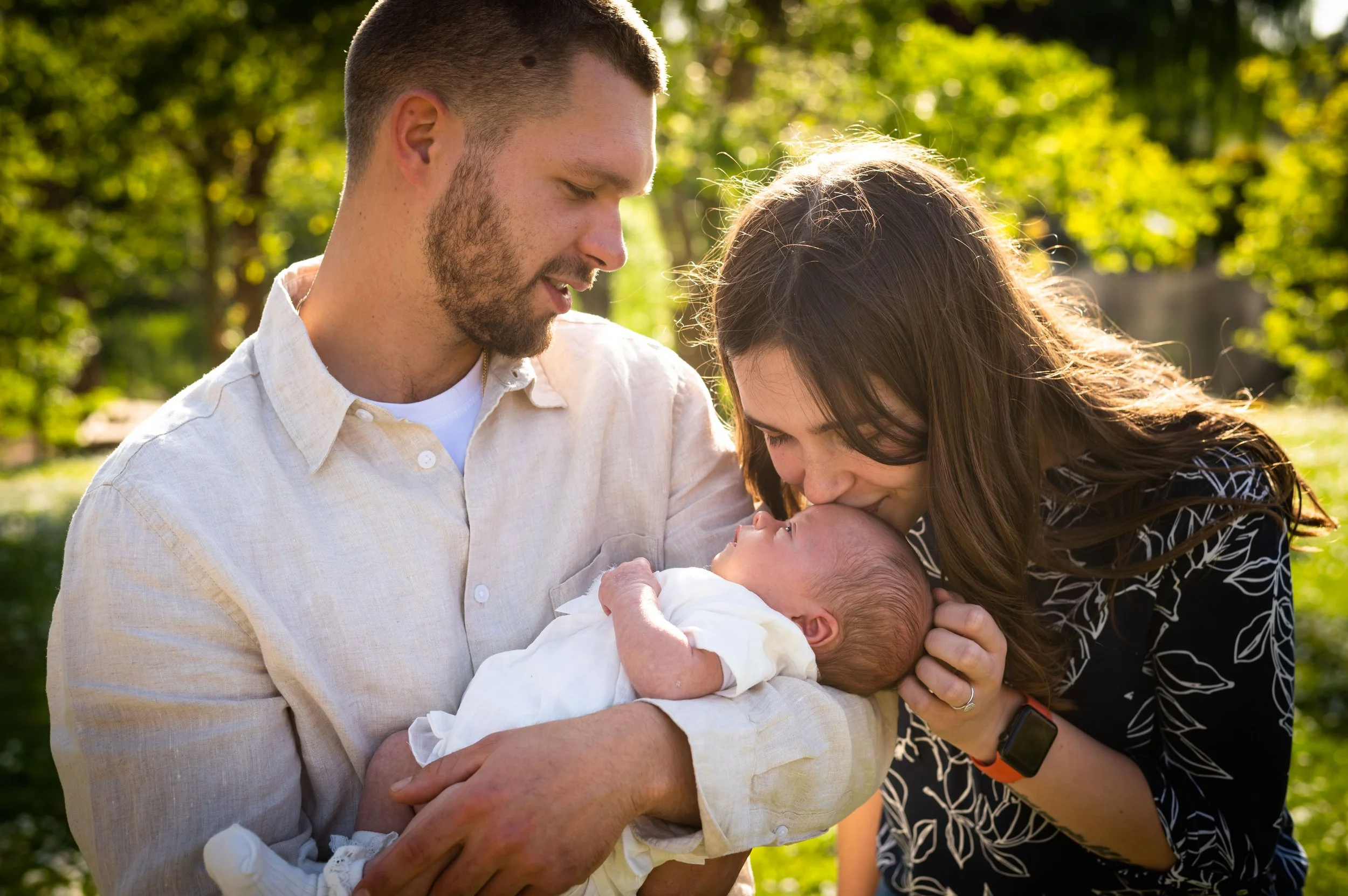 Een nieuwgeboren baby wordt door een man en een vrouw in de natuur gekust.