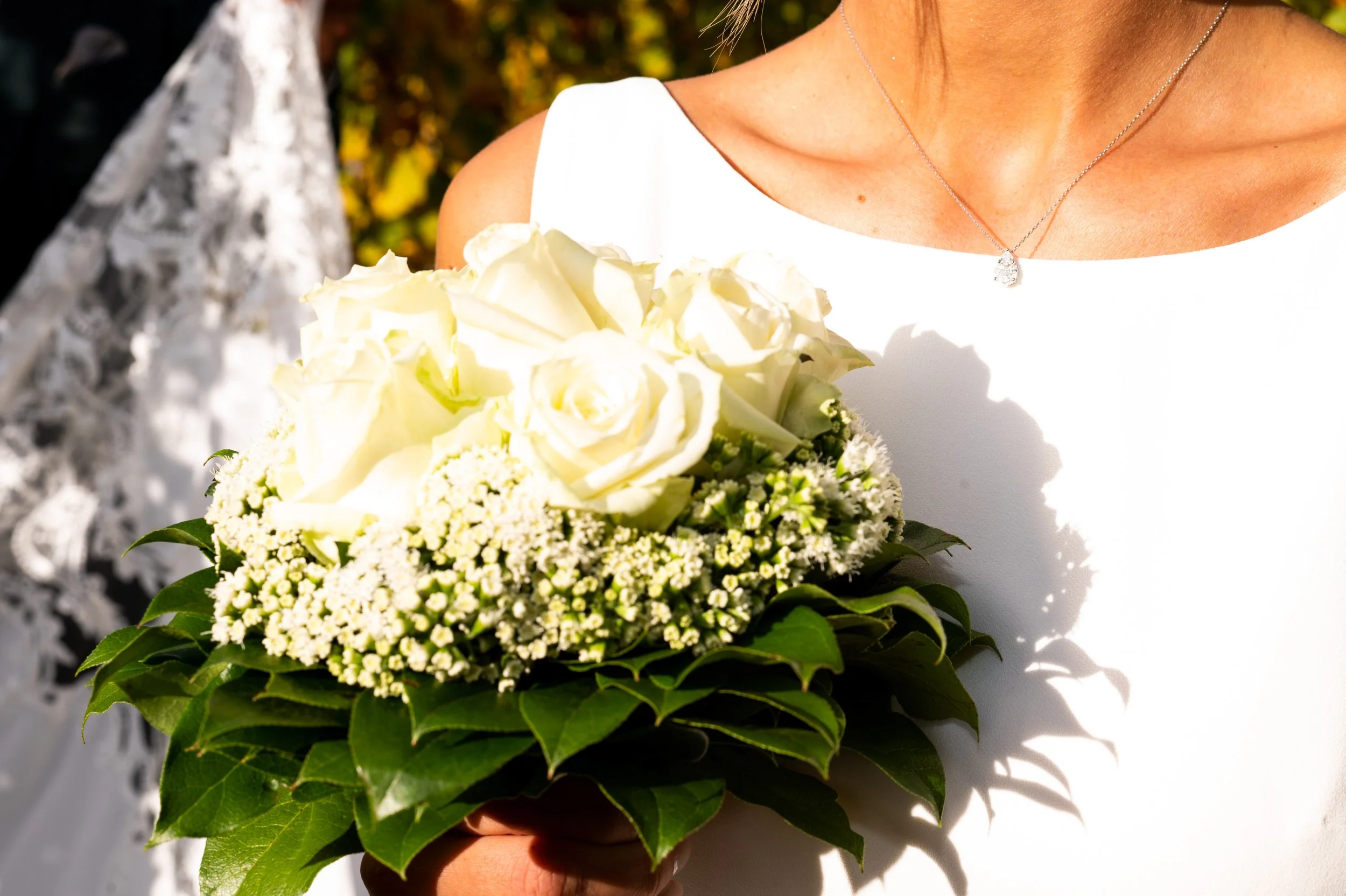 Close-up van een bruid die een boeket van witte rozen en kleine witte bloemen vasthoudt, met een witte jurk en een holografische achtergrond.