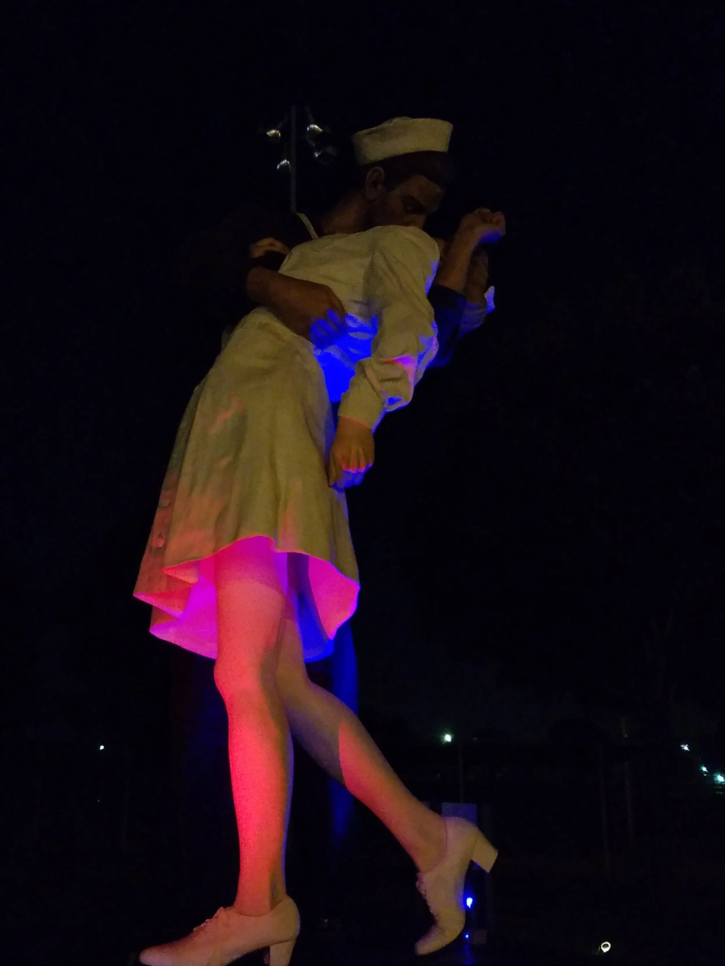 A huge statue of a man and a woman kissing, illuminated by LED lights from the bottom.