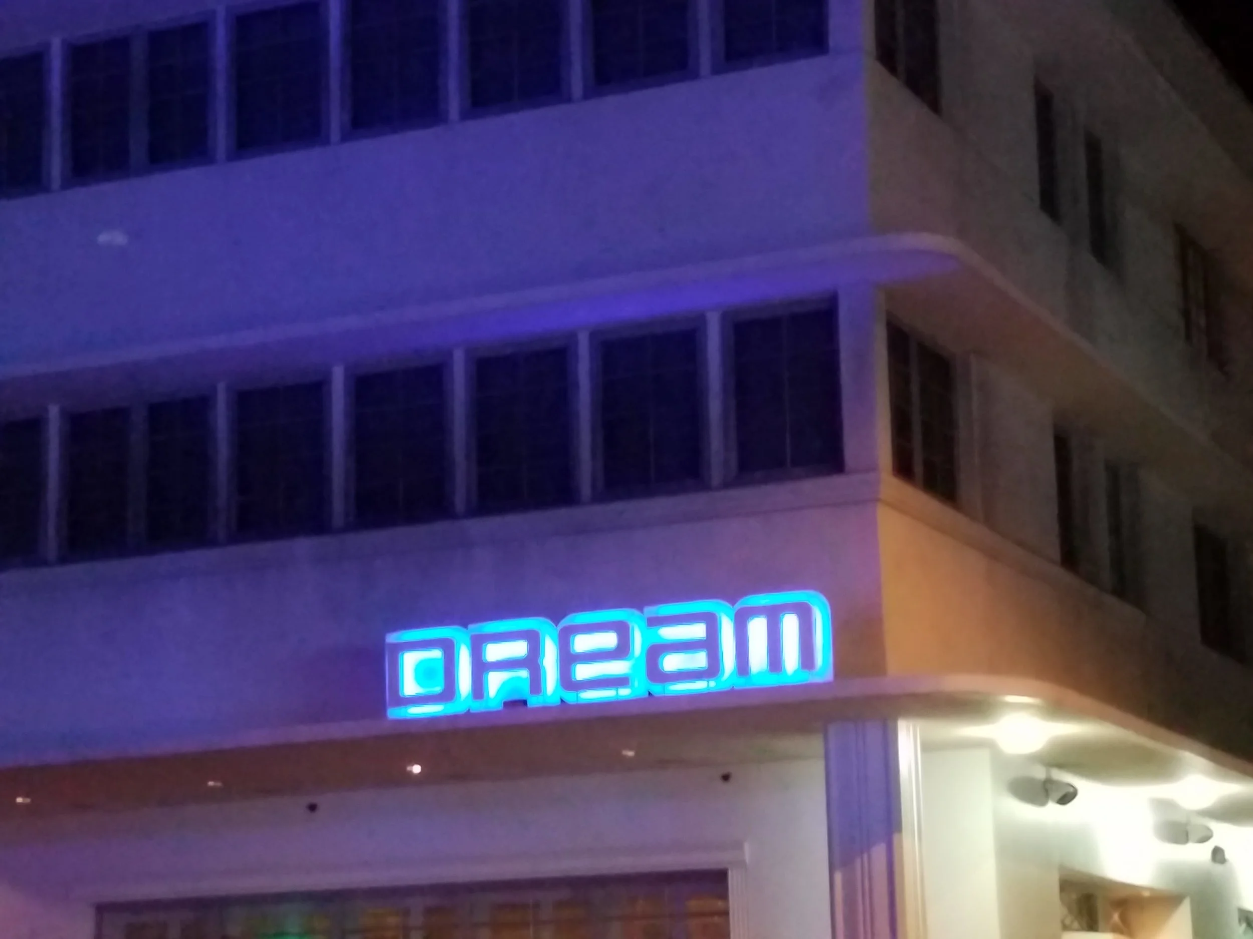 Neon blue sign reading 'DREAM' on the side of a building at night.