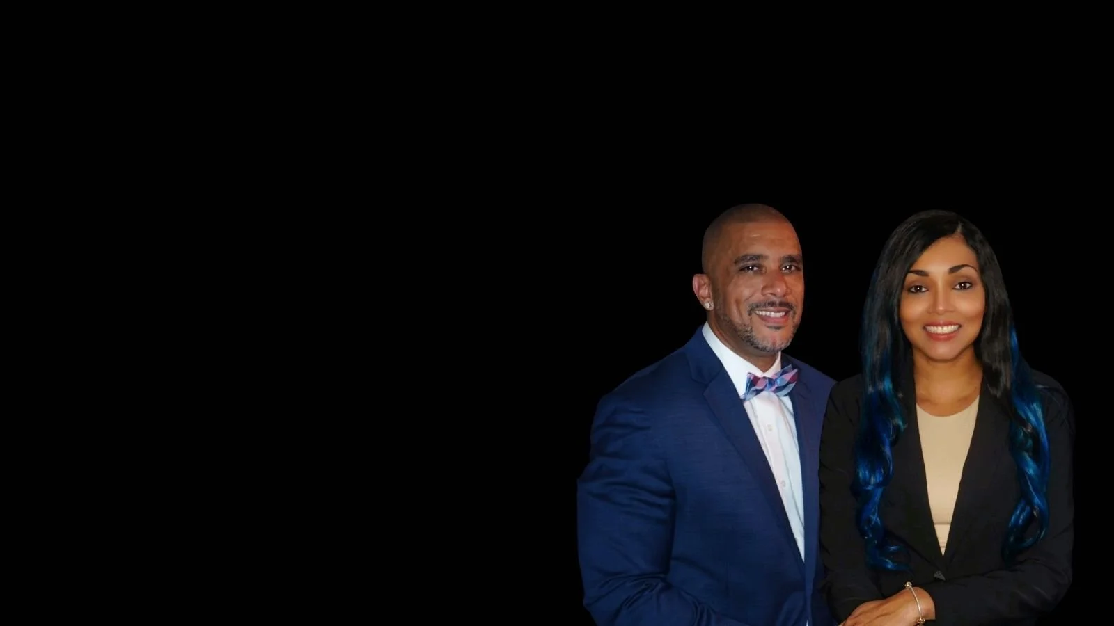 A man in a blue suit with a bow tie and a woman with long black and blue hair smiling against a black background.