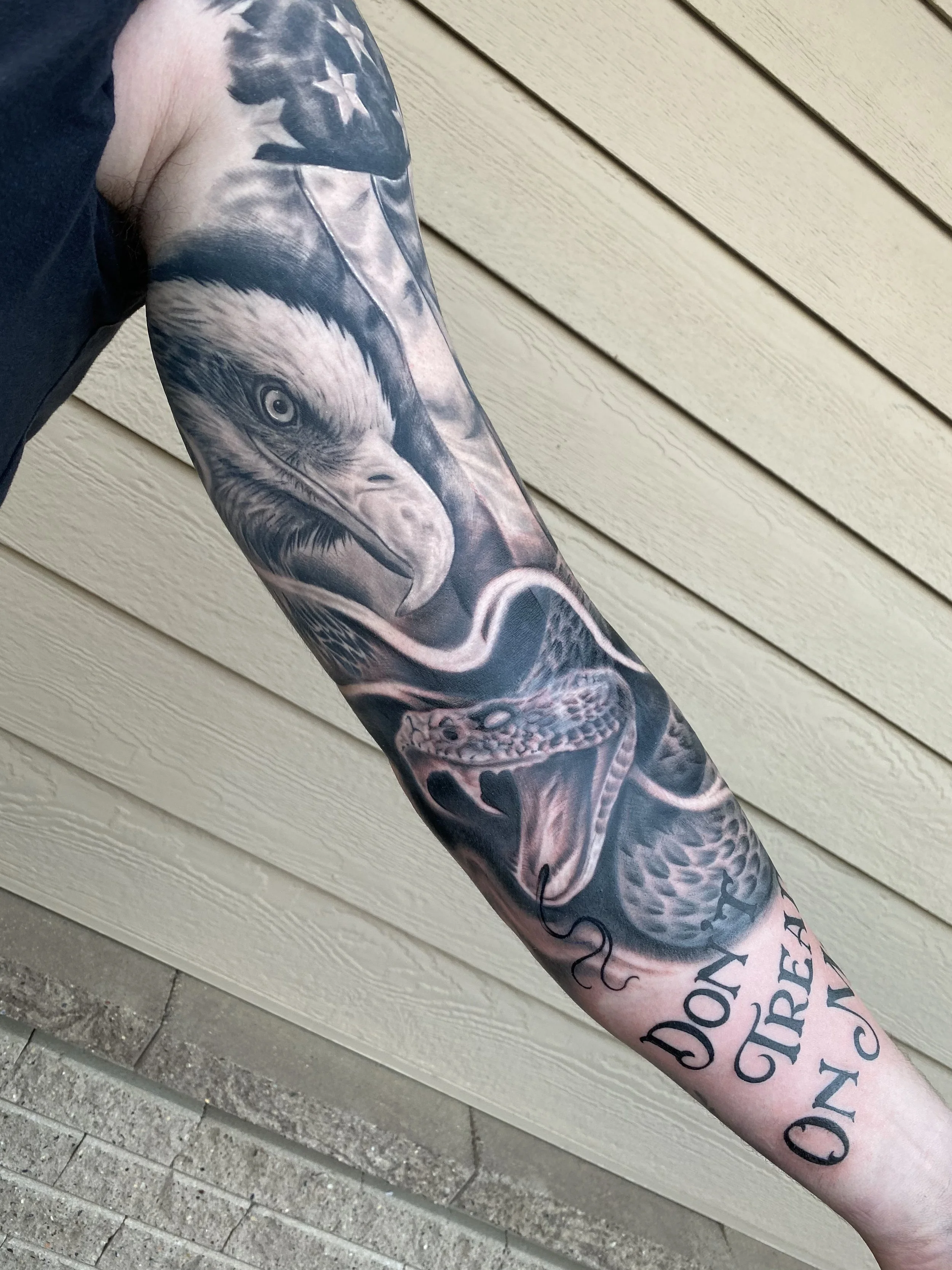 Tattoo sleeve on a person's arm depicting a bald eagle and a snake with the phrase "DON'T TREAD ON ME".