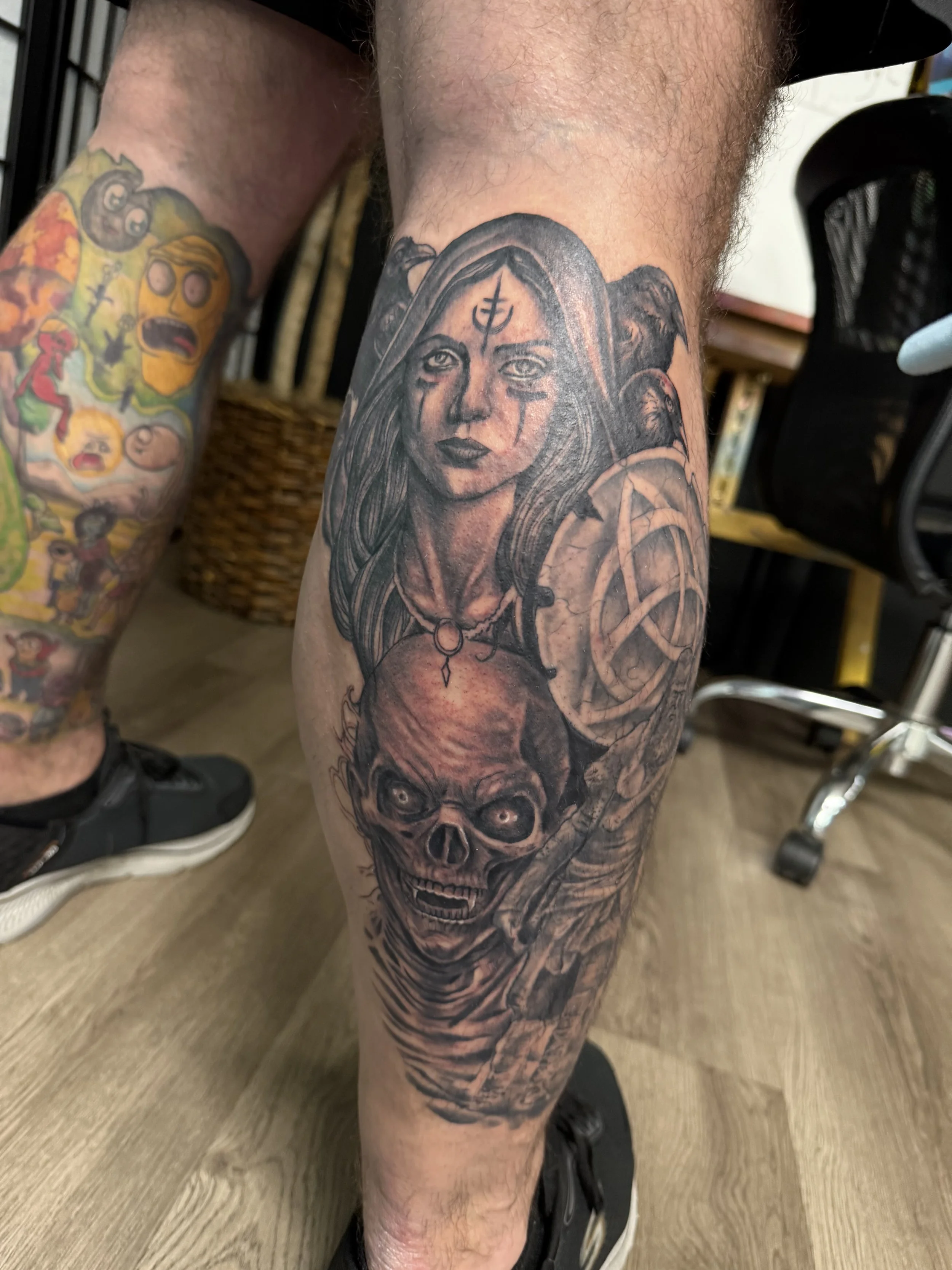 Sioux Falls South Dakota Tattoo Shop. Apex Ink. Tattoo of a woman with long hair and face paint, holding a skull with an eerie expression, surrounded by dark imagery.