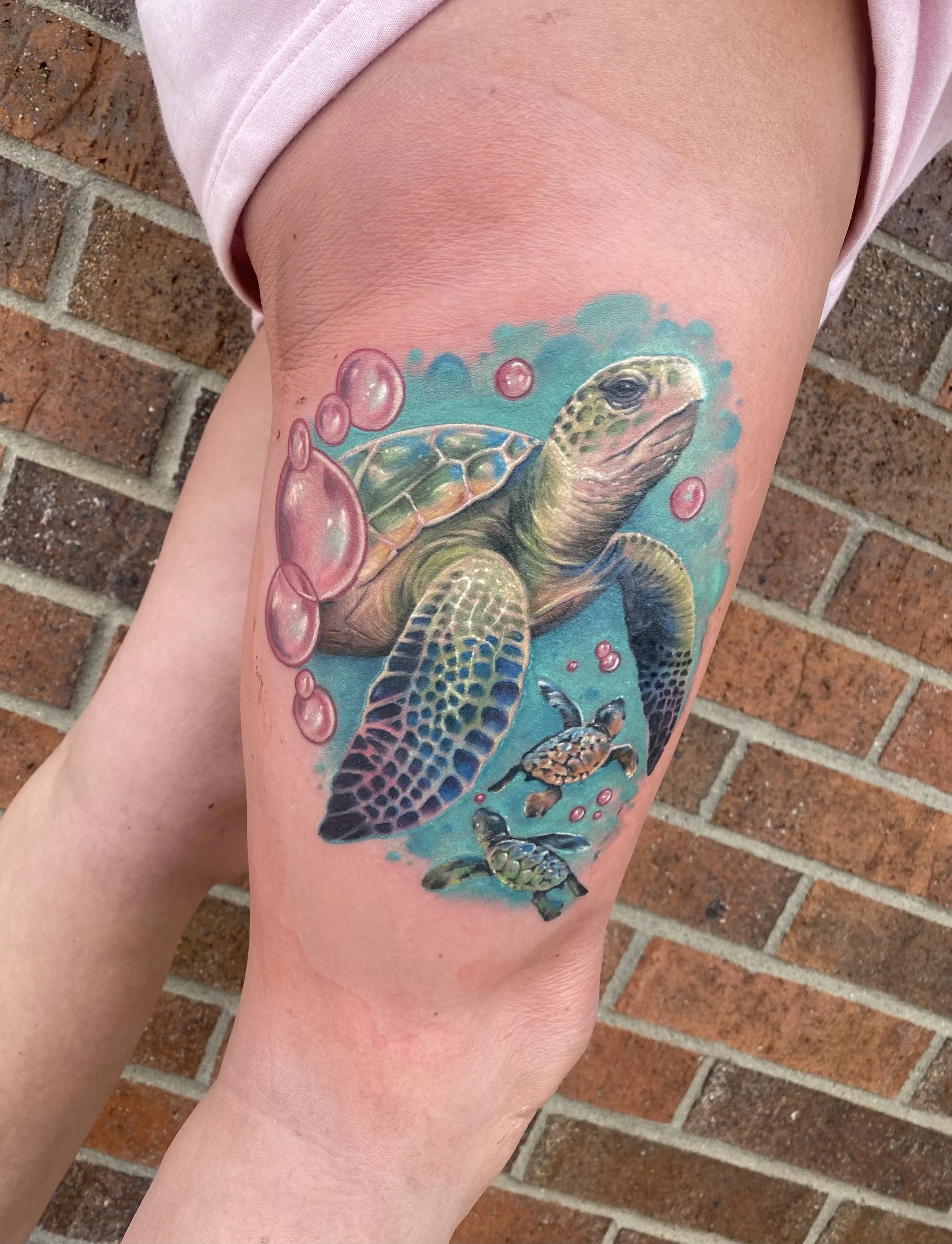 Colorful tattoo of a turtle swimming underwater with bubbles and smaller sea turtles, set against a blue background.