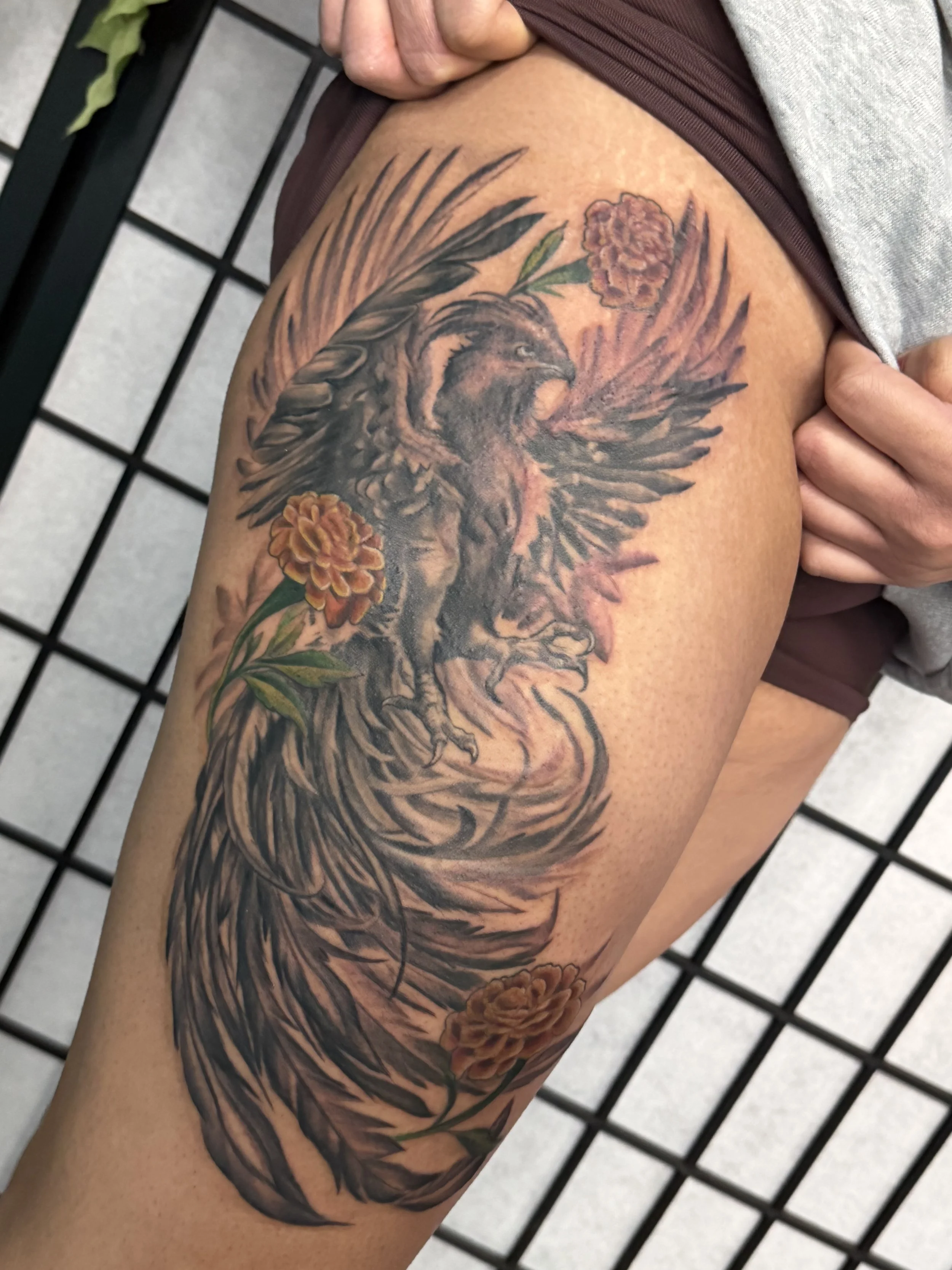 Sioux Falls South Dakota Tattoo Shop. Apex Ink. Tattoo of a stylized eagle with outspread wings and detailed feathers, surrounded by three orange flowers with green leaves.