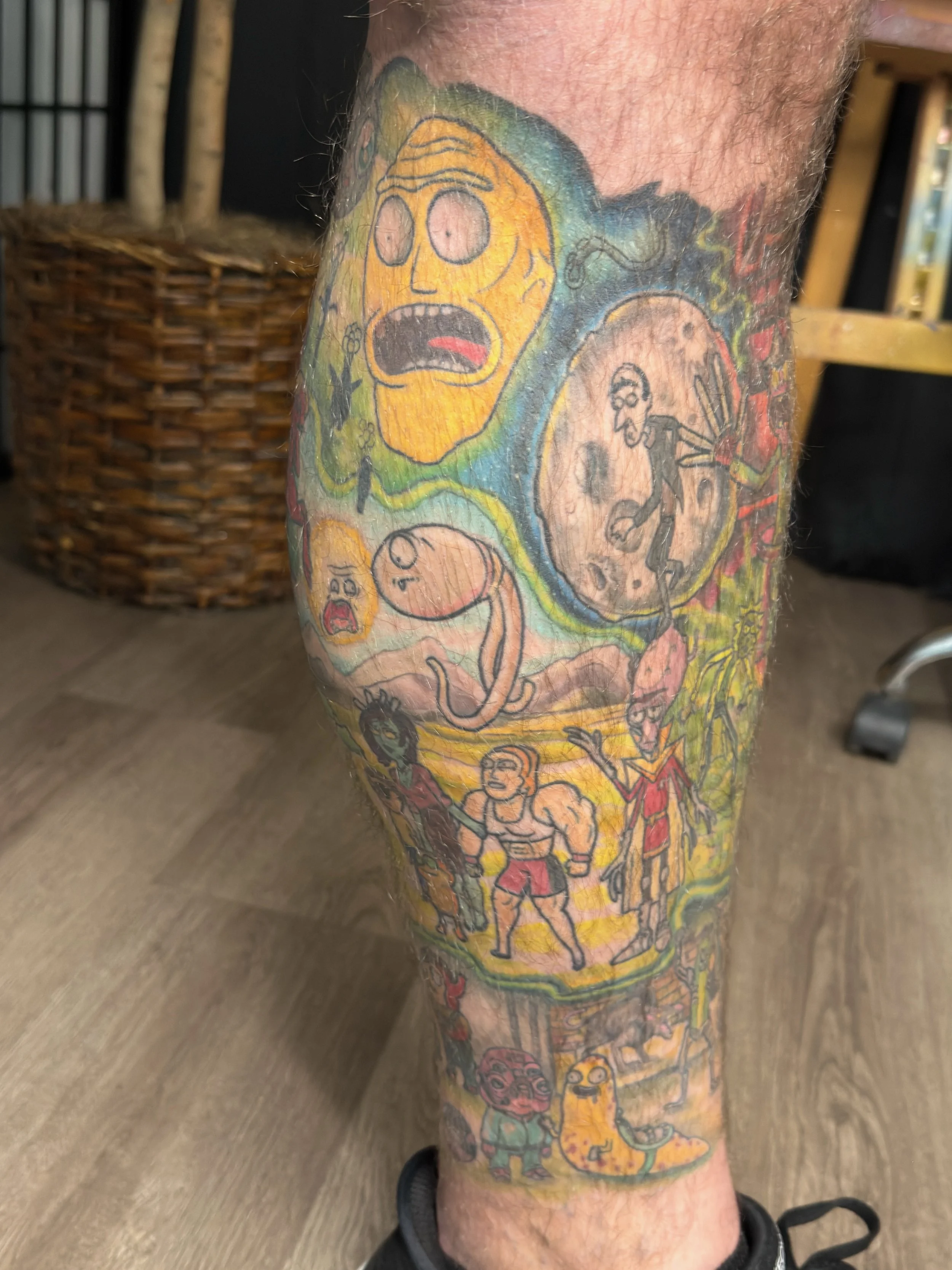 Sioux Falls South Dakota Tattoo Shop. Apex Ink. A colorful tattoo sleeve featuring various cartoon characters and scenes, including a surprised face, a walking figure, a snake, muscular man, and other whimsical designs.