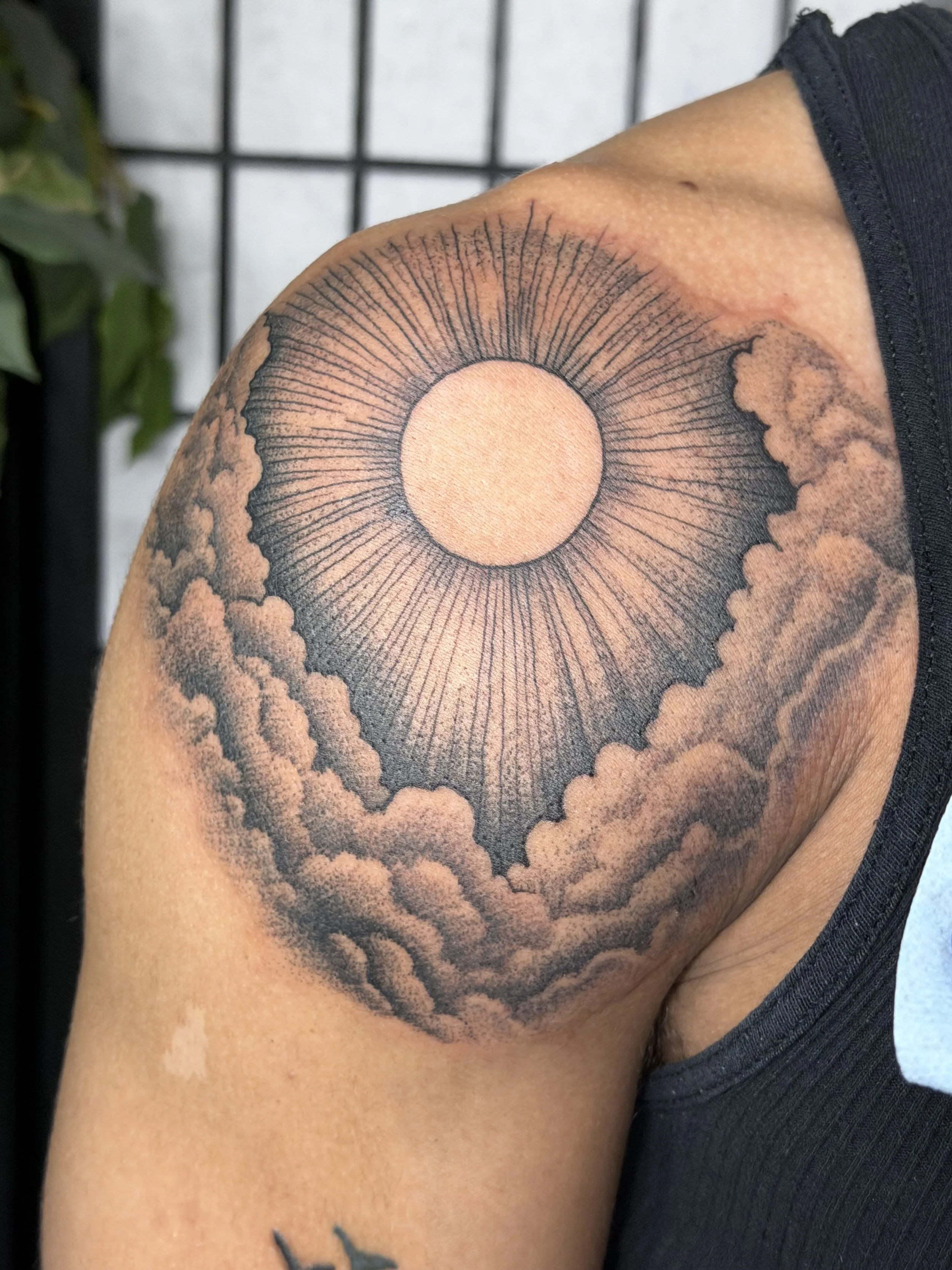 Sioux Falls South Dakota Tattoo Shop. Apex Ink. Tattoo of a sun with rays surrounded by clouds on the upper arm.