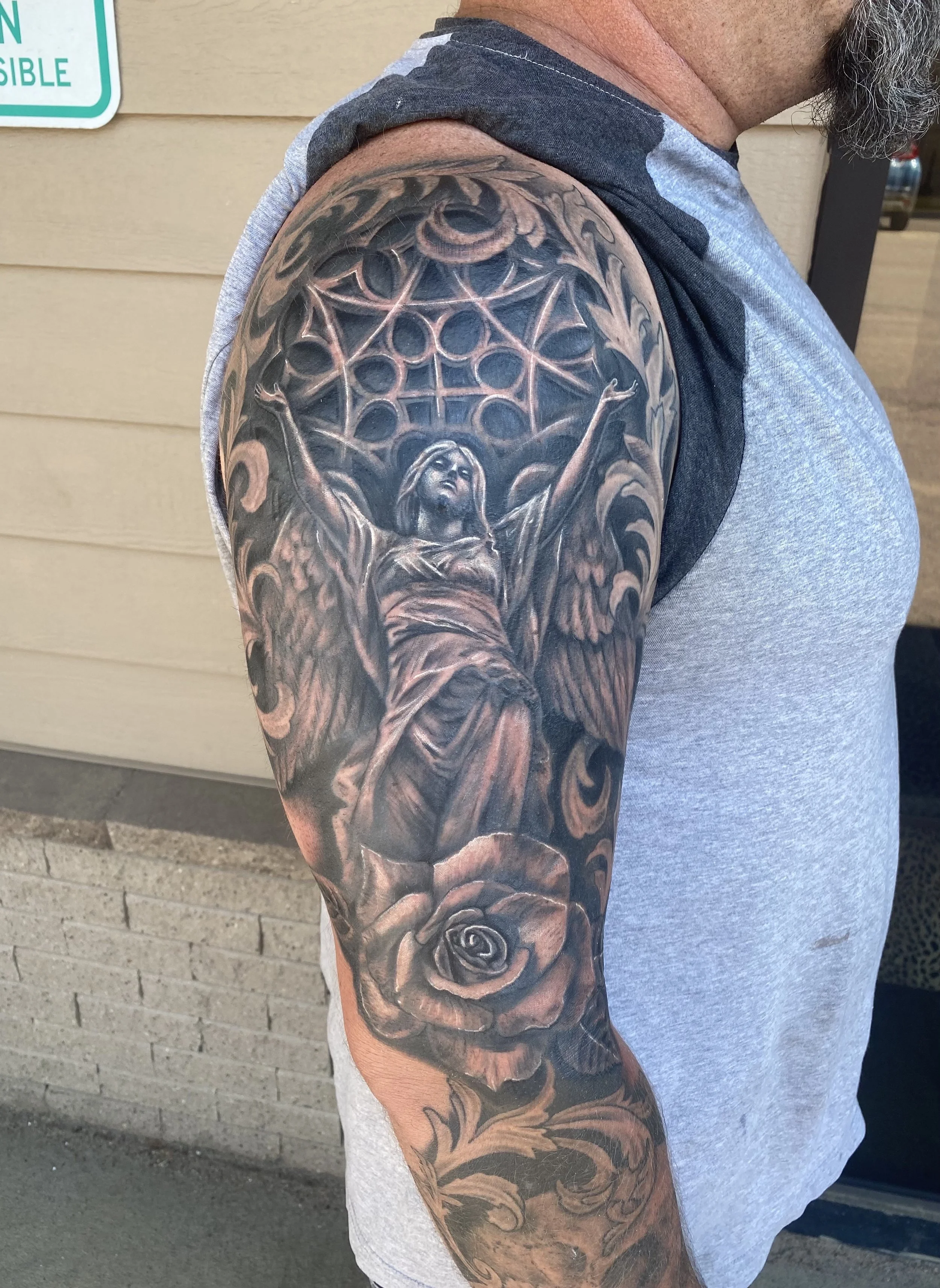 Black and gray arm tattoo featuring a woman with wings, surrounded by a geometric pattern and floral elements.