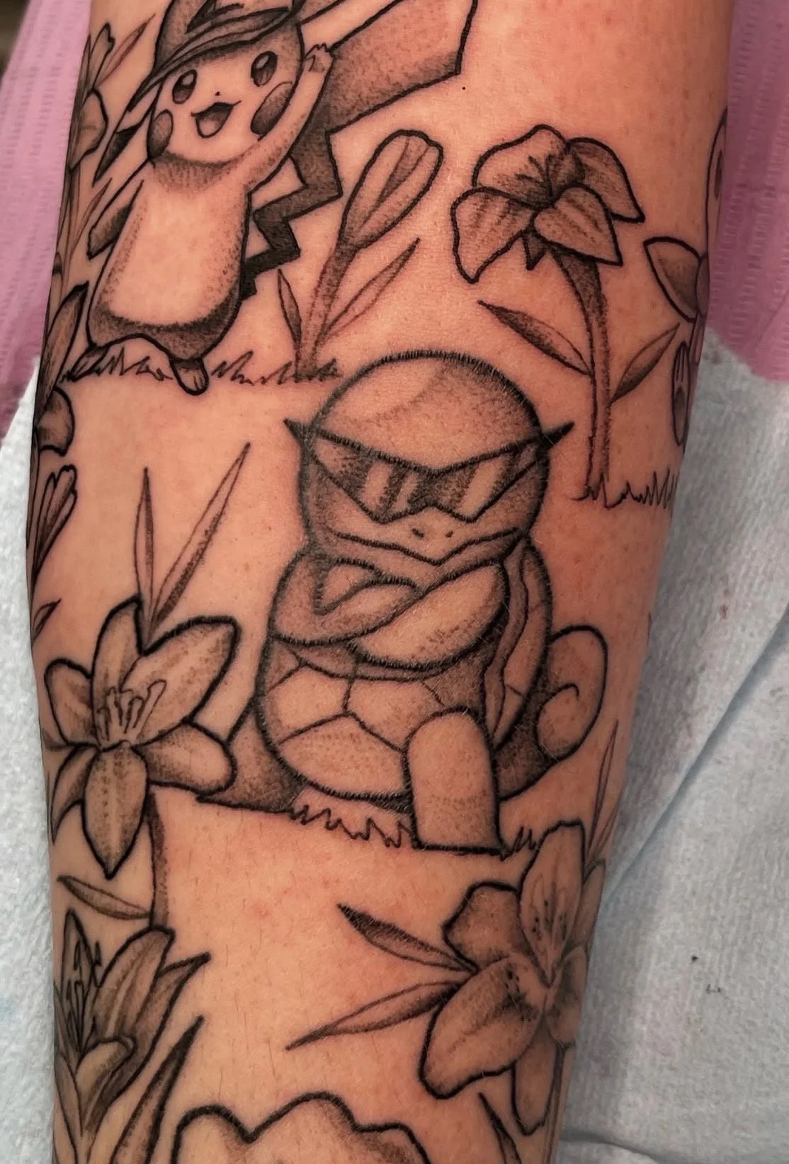 Sioux Falls South Dakota Tattoo Shop. Apex Ink. Tattoo featuring Pokémon characters Pikachu and Squirtle among flowers and leaves.