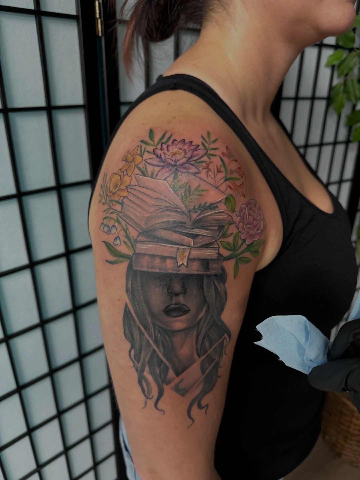 Sioux Falls South Dakota Tattoo Shop. Apex Ink. Tattoo of a woman's face with long hair, with an open book and flowers above her head on her upper arm.