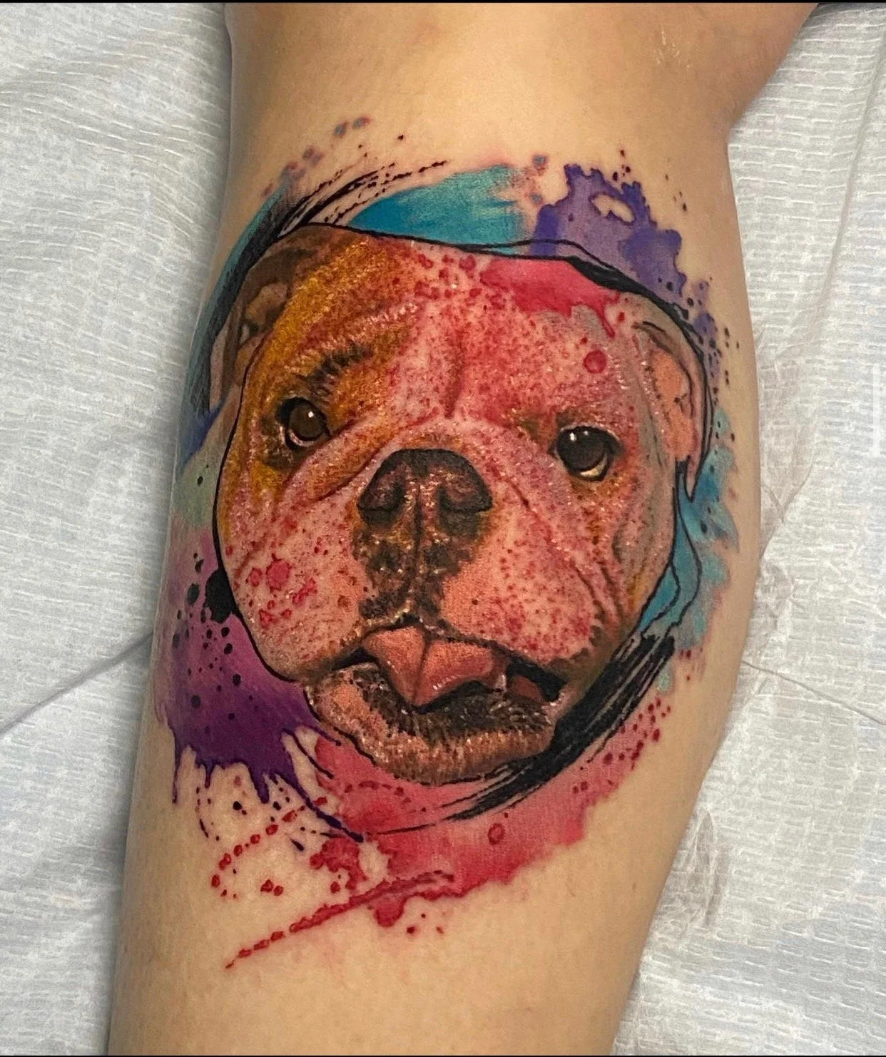 Watercolor-style tattoo of a dog's face with a colorful background.