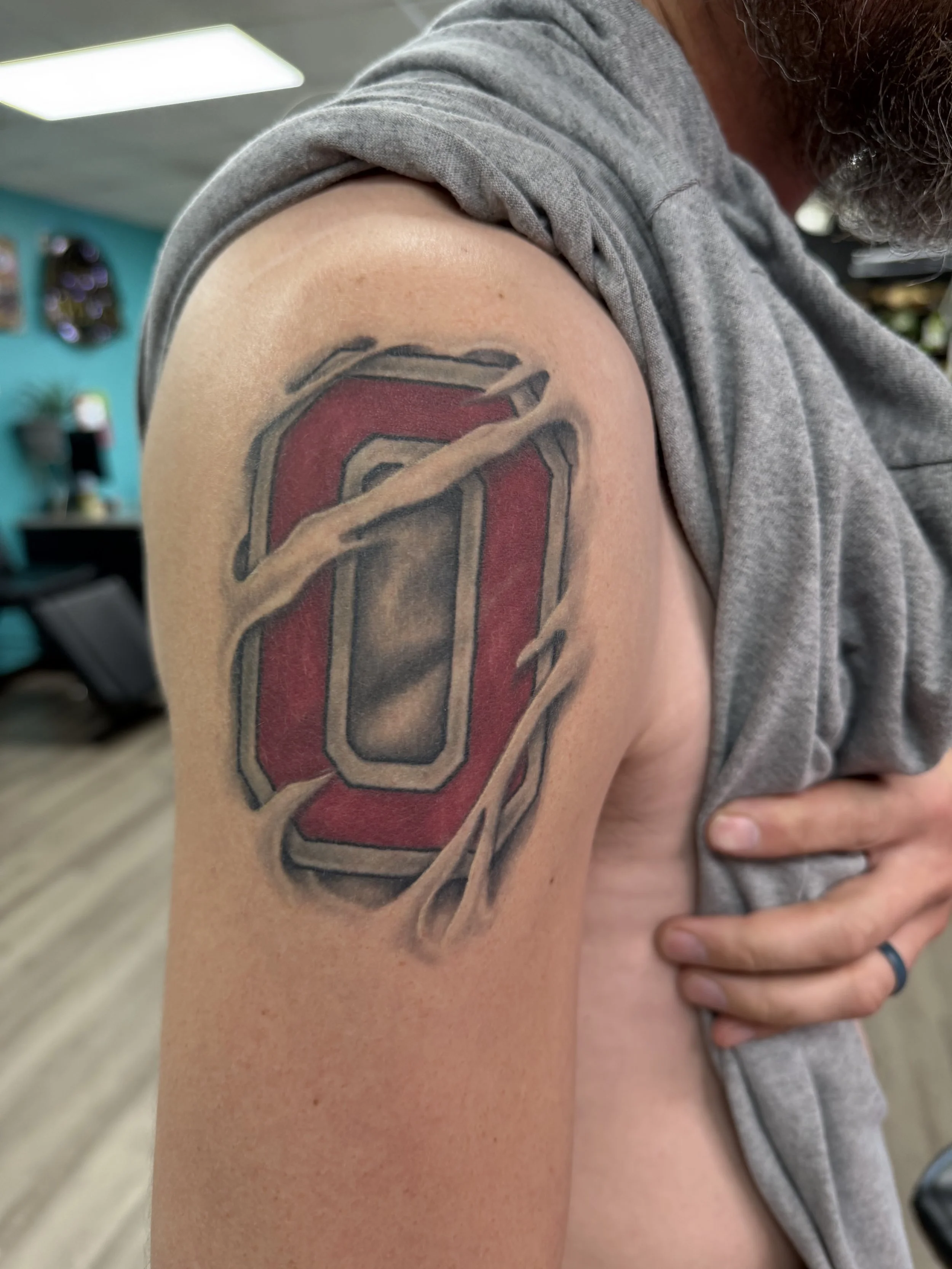 Sioux Falls South Dakota Tattoo Shop. Apex Ink. Tattoo of a large red and black Oklahoma Sooners logo with a cracked, 3D effect on upper arm