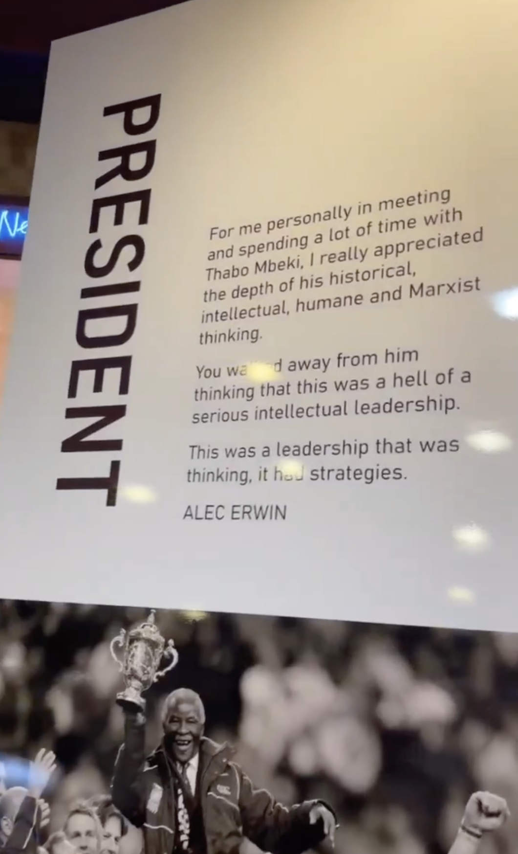A poster with the title 'PRESIDENT' and a quote by Alec Erwin is displayed above a black and white photograph of Nelson Mandela celebrating with a trophy in his right hand. The quote discusses admiration for Thabo Mbeki's historical, intellectual, humane, and Marxist thinking.